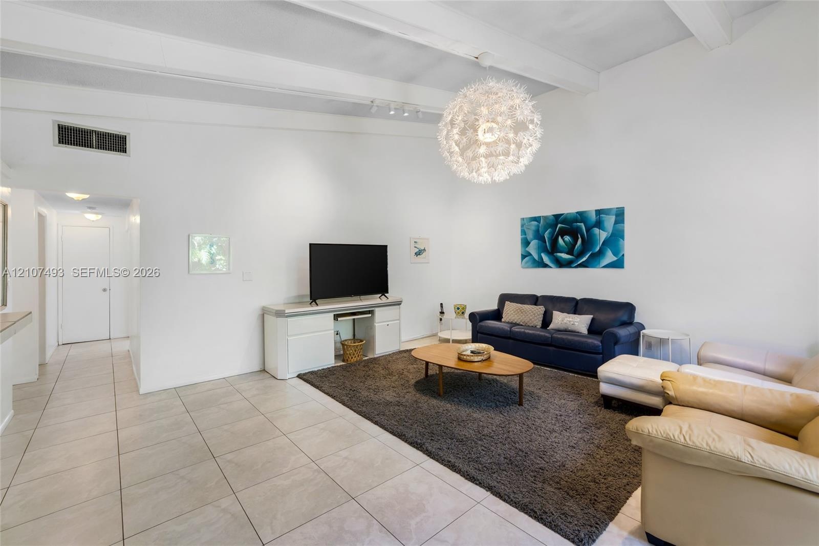 Vaulted ceilings with exposed beams, large spherical chandelier, and ceramic tile flooring