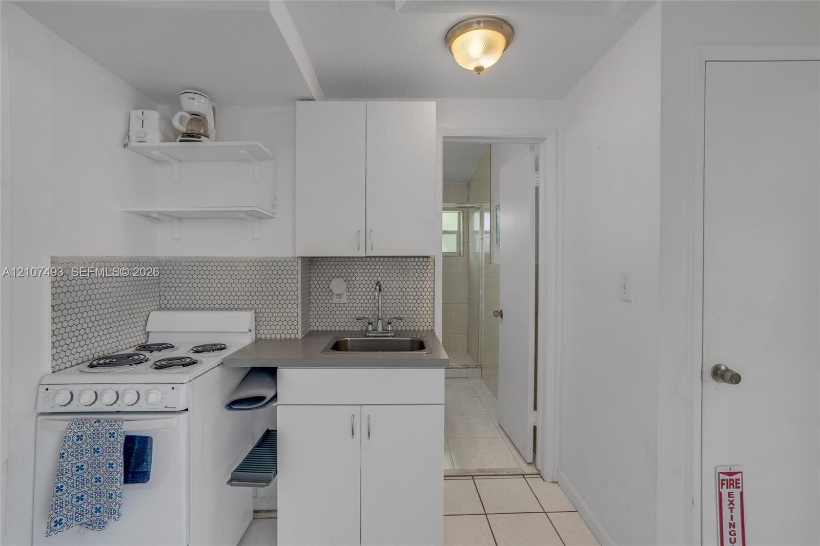 Kitchenette featuring white cabinetry, a neutral-toned countertop, a hexagonal tile backsplash, a white four-burner gas range, and a drop-in sink