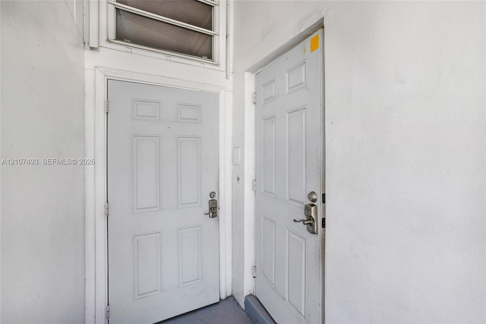 Two panel-style doors with metallic lever handles, deadbolt locks, and an integrated transom window above the left entrance