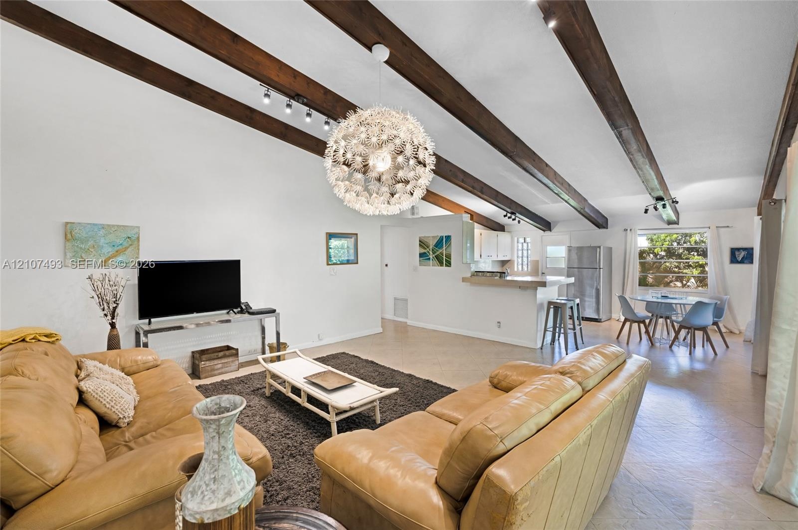 Vaulted ceilings featuring exposed wood beams, a contemporary sputnik-style chandelier, track lighting, and tile flooring
