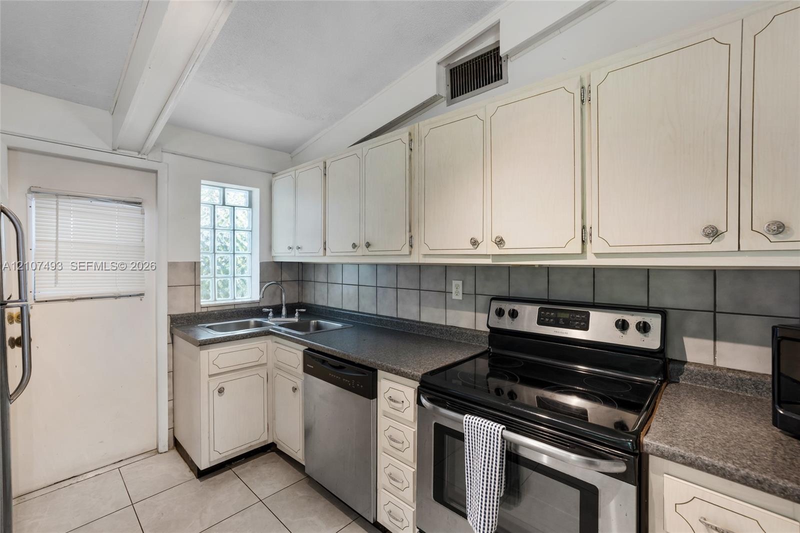 Kitchen featuring white cabinetry, dark stone-finish countertops, stainless steel appliances, a square glass block window, and tile flooring