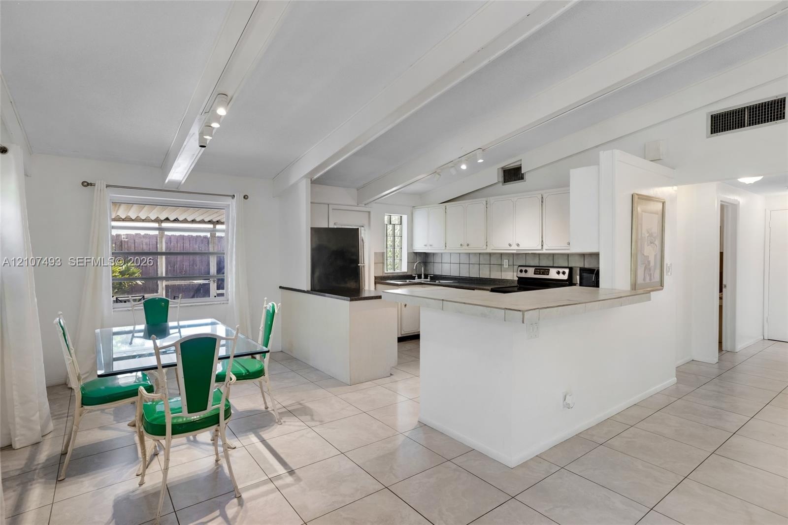Vaulted ceilings with exposed beams, tile flooring, breakfast bar, and track lighting