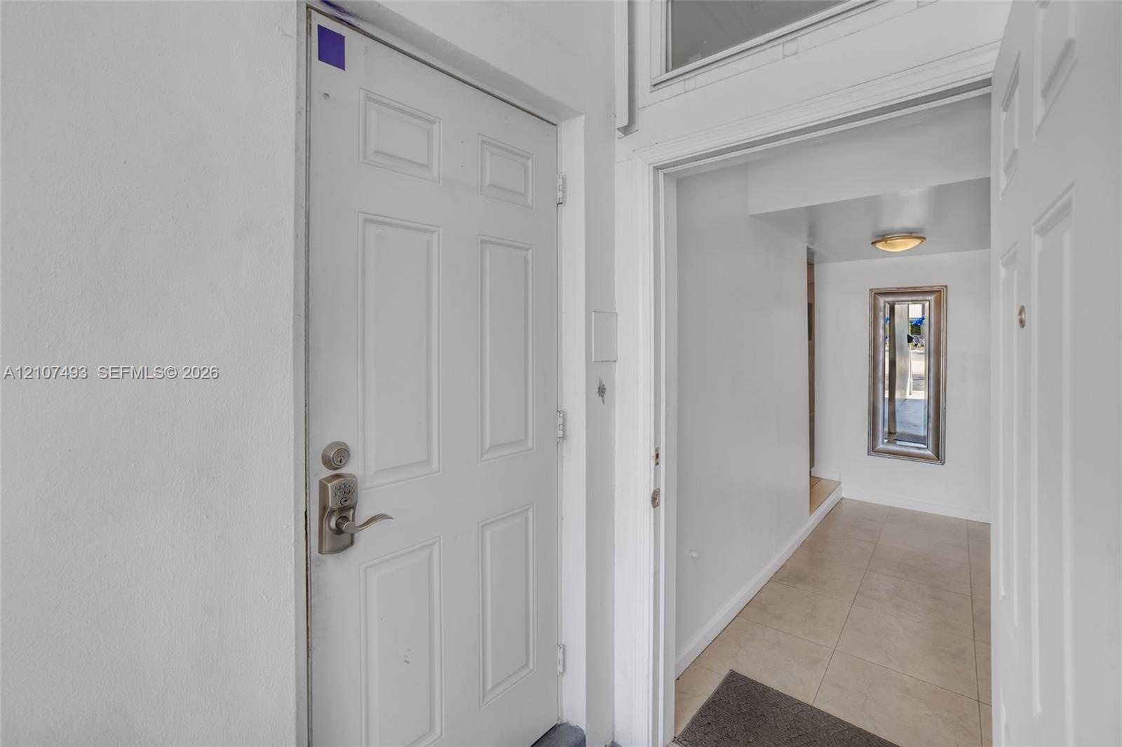 Six-panel interior door with satin nickel hardware, transom window, and neutral tile flooring