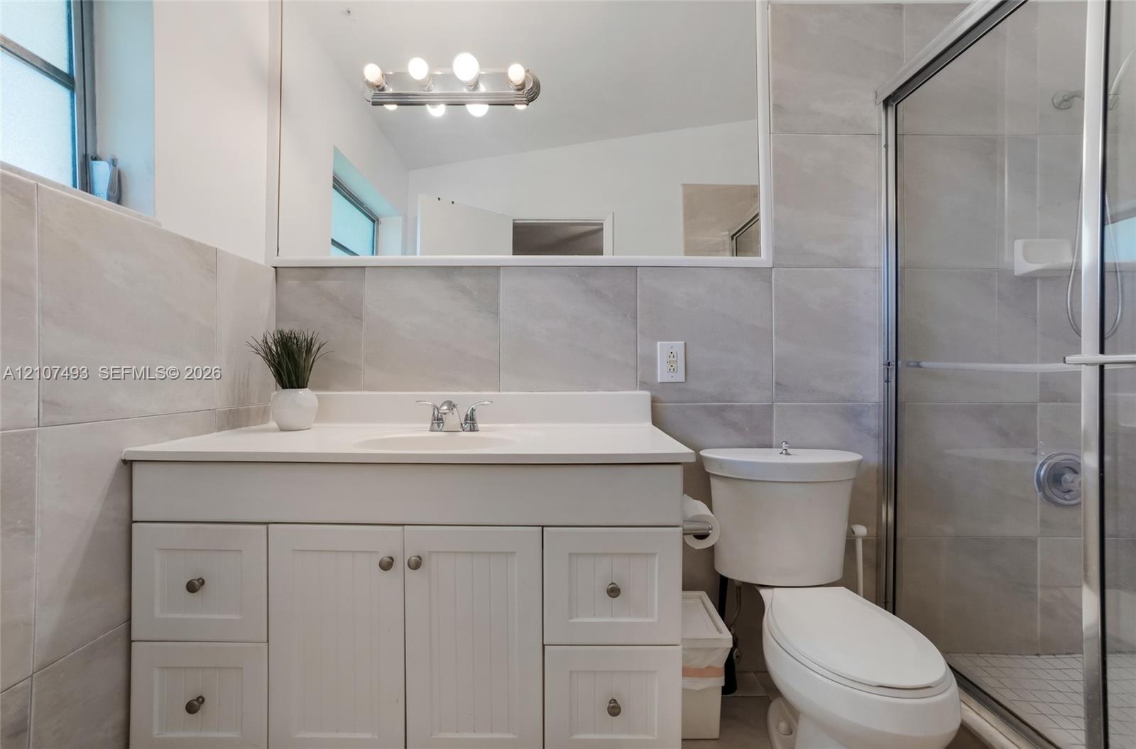 Bathroom featuring a white vanity cabinet, solid-surface countertop with integrated sink, large-format tile wall cladding, full-width mirror, and a gl
