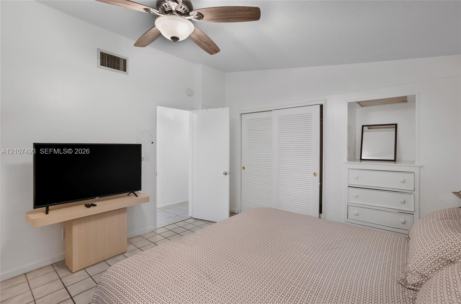 Room featuring vaulted ceilings, neutral ceramic tile flooring, ceiling fan with integrated lighting, built-in wooden shelving, and a closet with louv