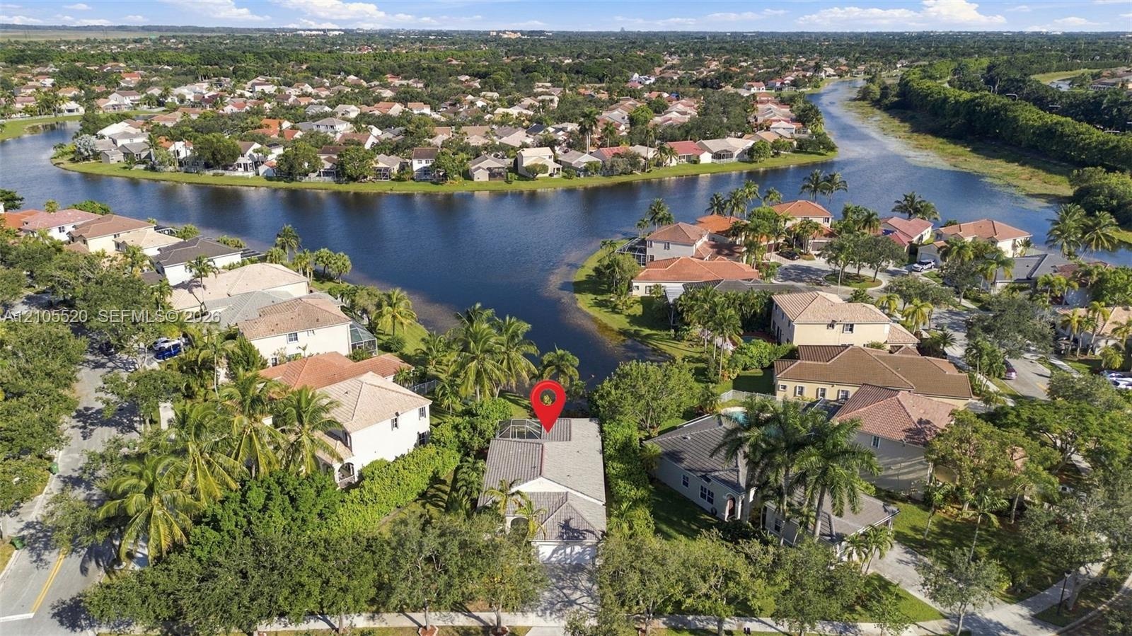 Aerial perspective of a waterfront residential property featuring an enclosed lanai and established landscaping