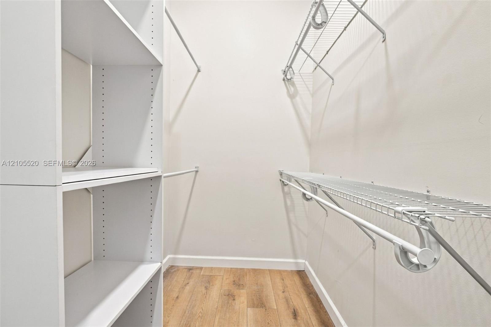 Walk-in storage space featuring wood-finish flooring, white laminate shelving towers, and white wire rack shelving with integrated hanging rods