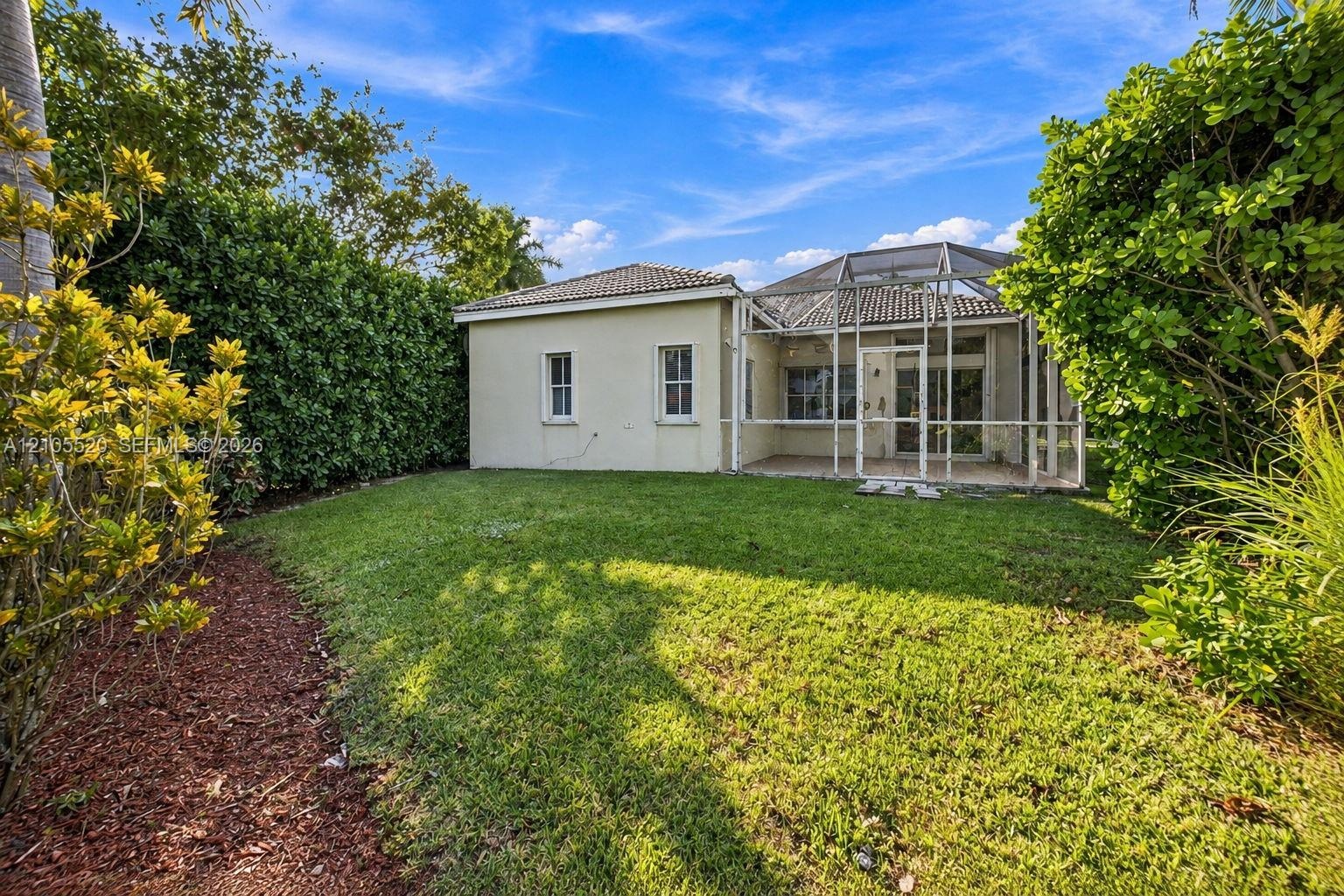 Rear exterior featuring a screened-in lanai, concrete tile roof, manicured lawn, and perimeter landscaping