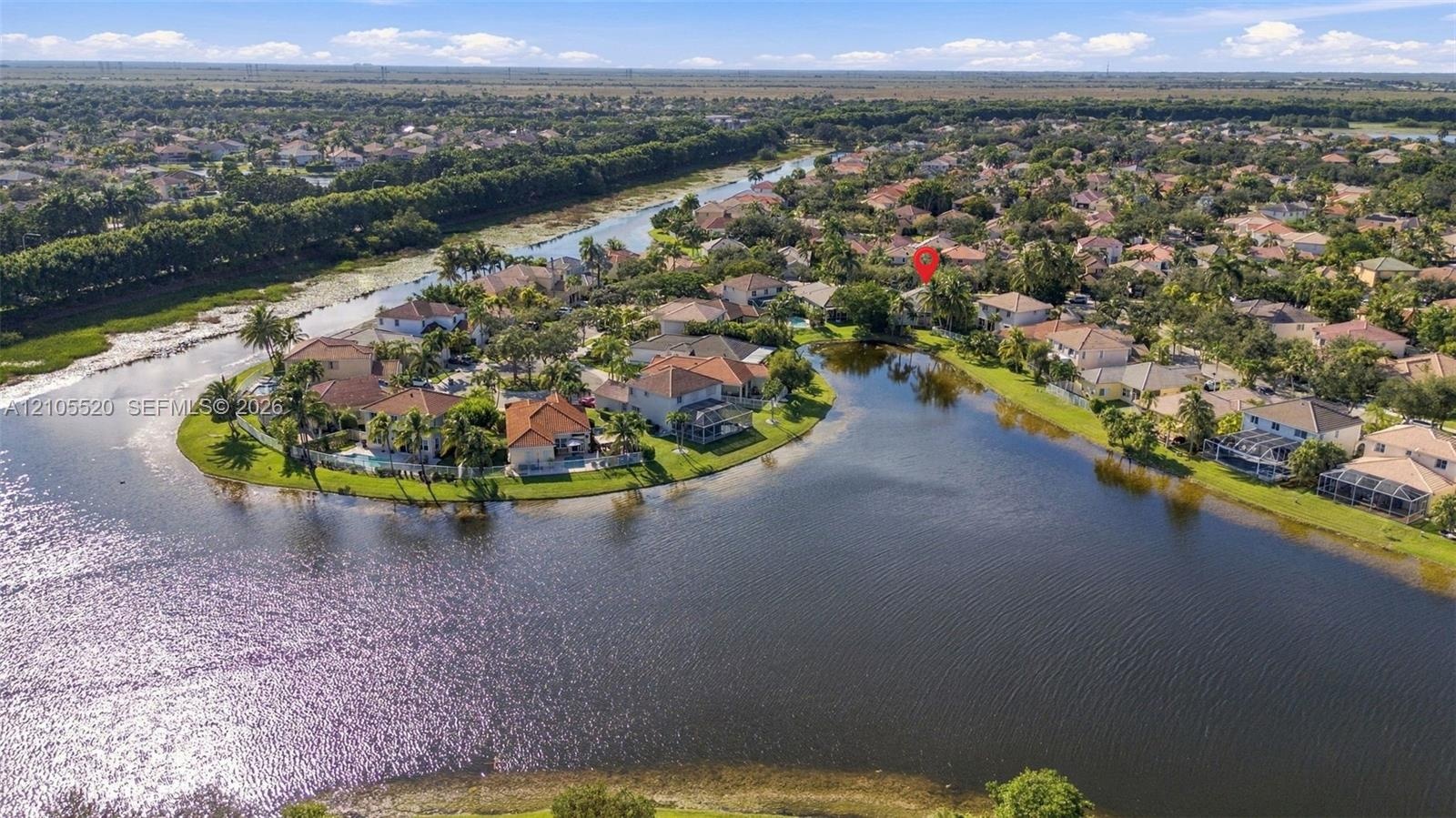Aerial perspective of a waterfront property featuring a tile roof, paved driveway, and expansive rear water frontage