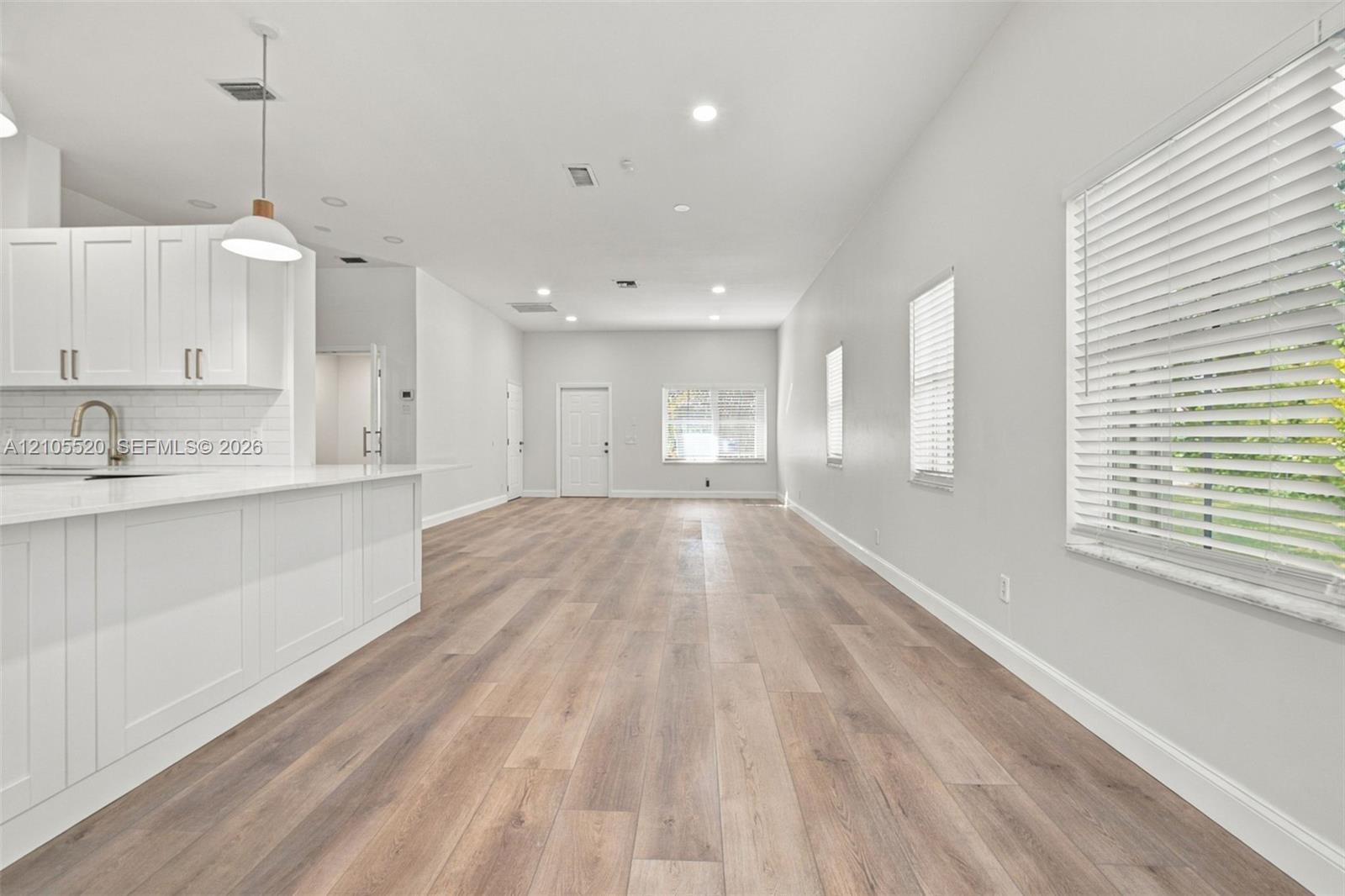 Open-concept interior featuring wood-finish flooring, white shaker-style cabinetry, a quartz-topped island, recessed lighting, and horizontal window b