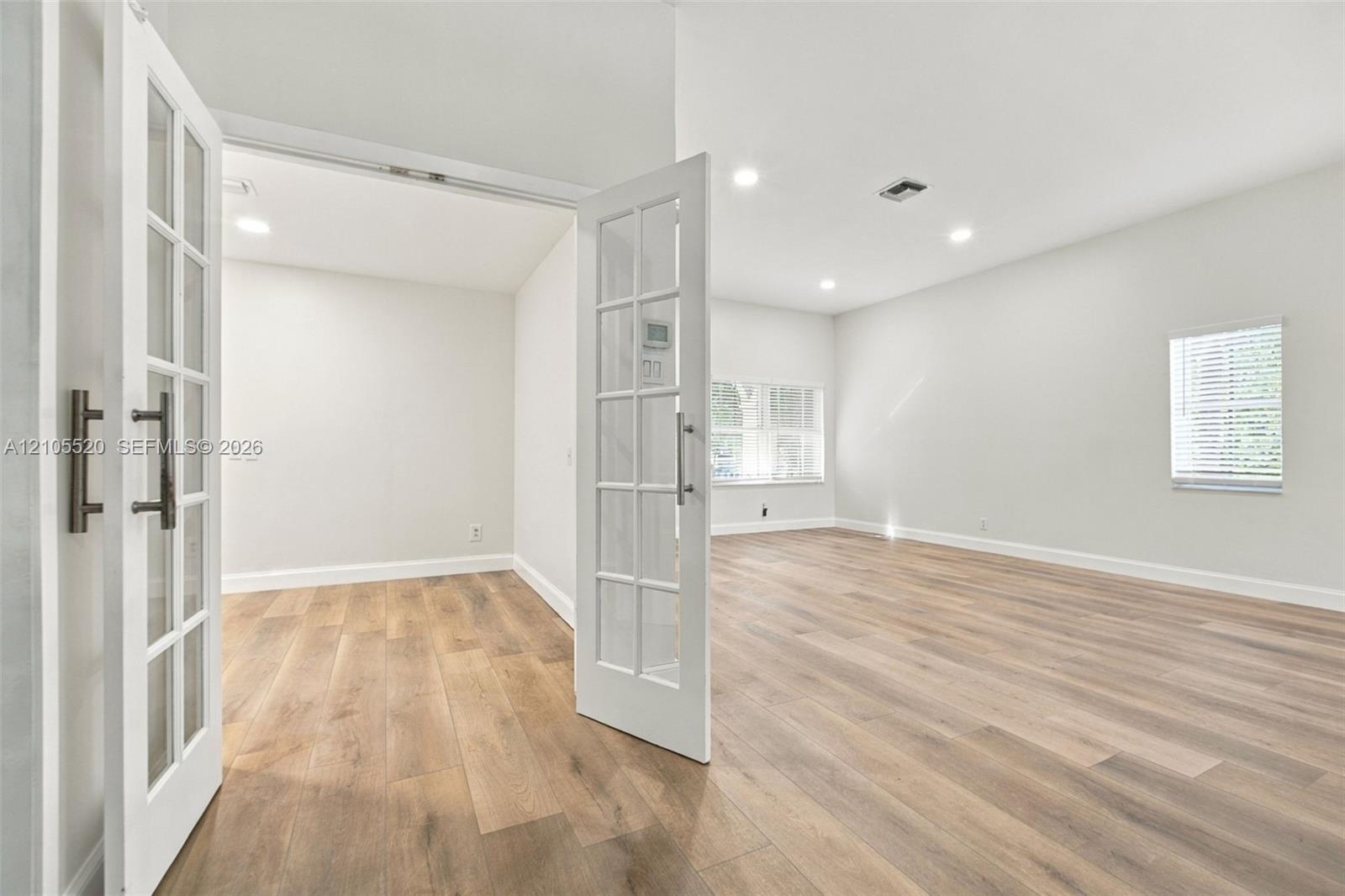 Wood-finish flooring, white French doors with glass panes, recessed lighting, and windows with horizontal blinds
