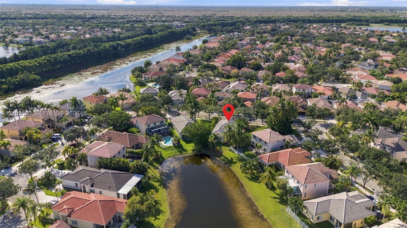 Aerial perspective of a multi-story residence featuring a tile roof, situated on a lot bordering a community pond with mature landscaping and palm tre