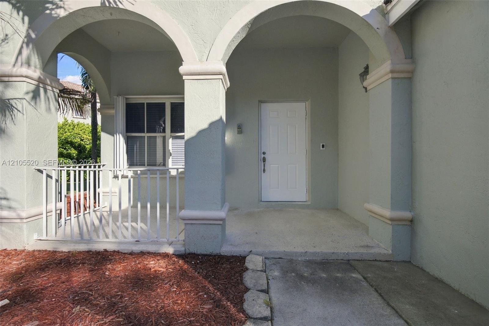 Covered entry porch featuring arched architectural detailing, stucco pillars, a white paneled front door, and a white metal balustrade