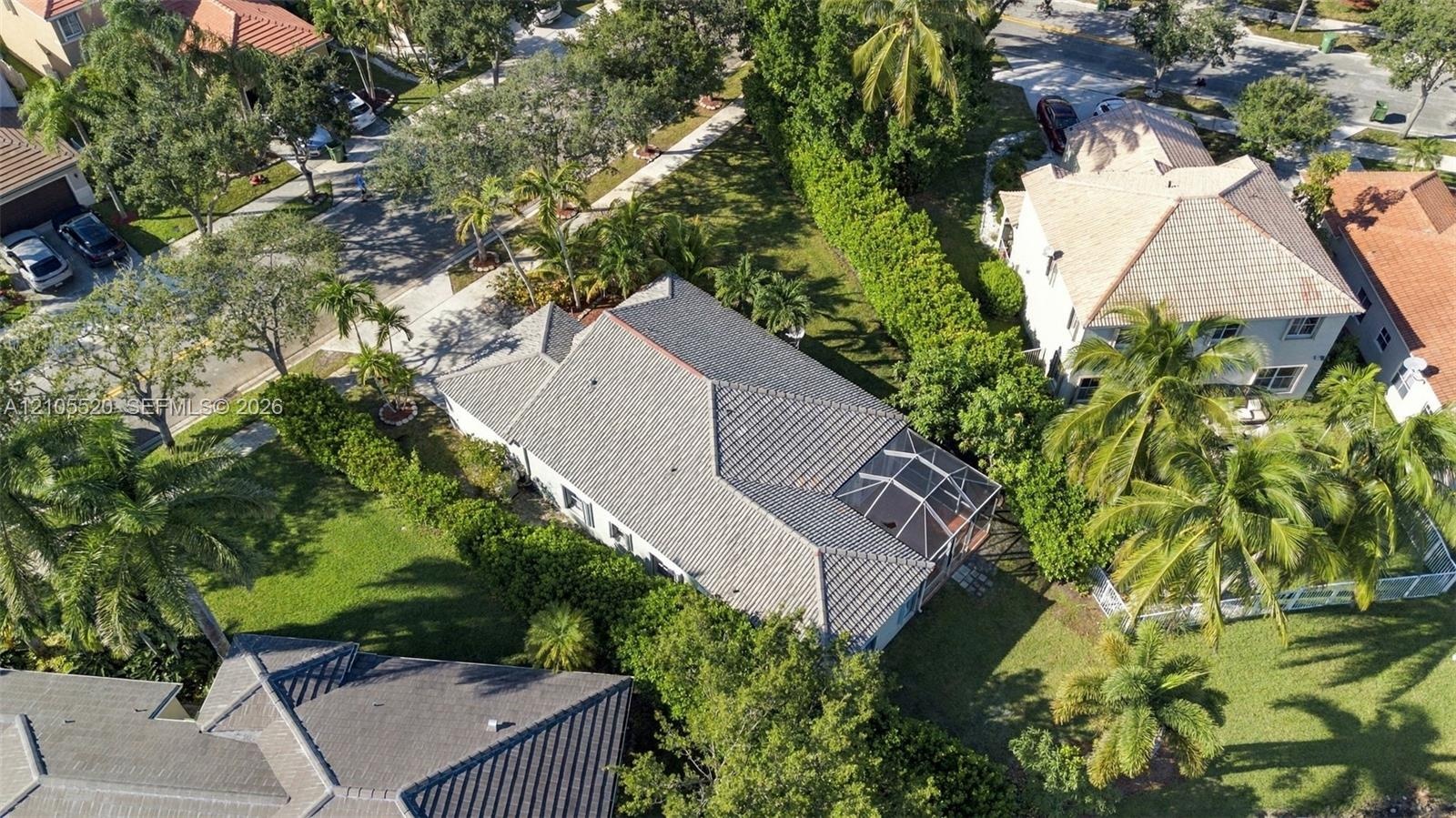 Aerial perspective of a property featuring a multi-pitched tile roof, an enclosed screened lanai, mature landscaping, and an expansive lawn