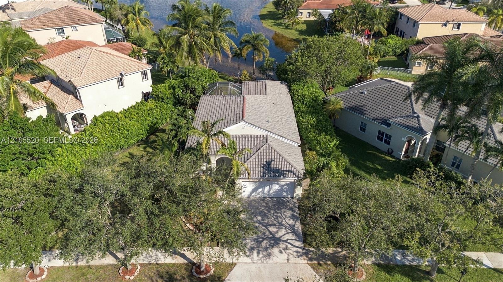 Aerial perspective featuring a concrete tile roof, paved driveway, enclosed rear patio, and mature landscaping on a waterfront lot