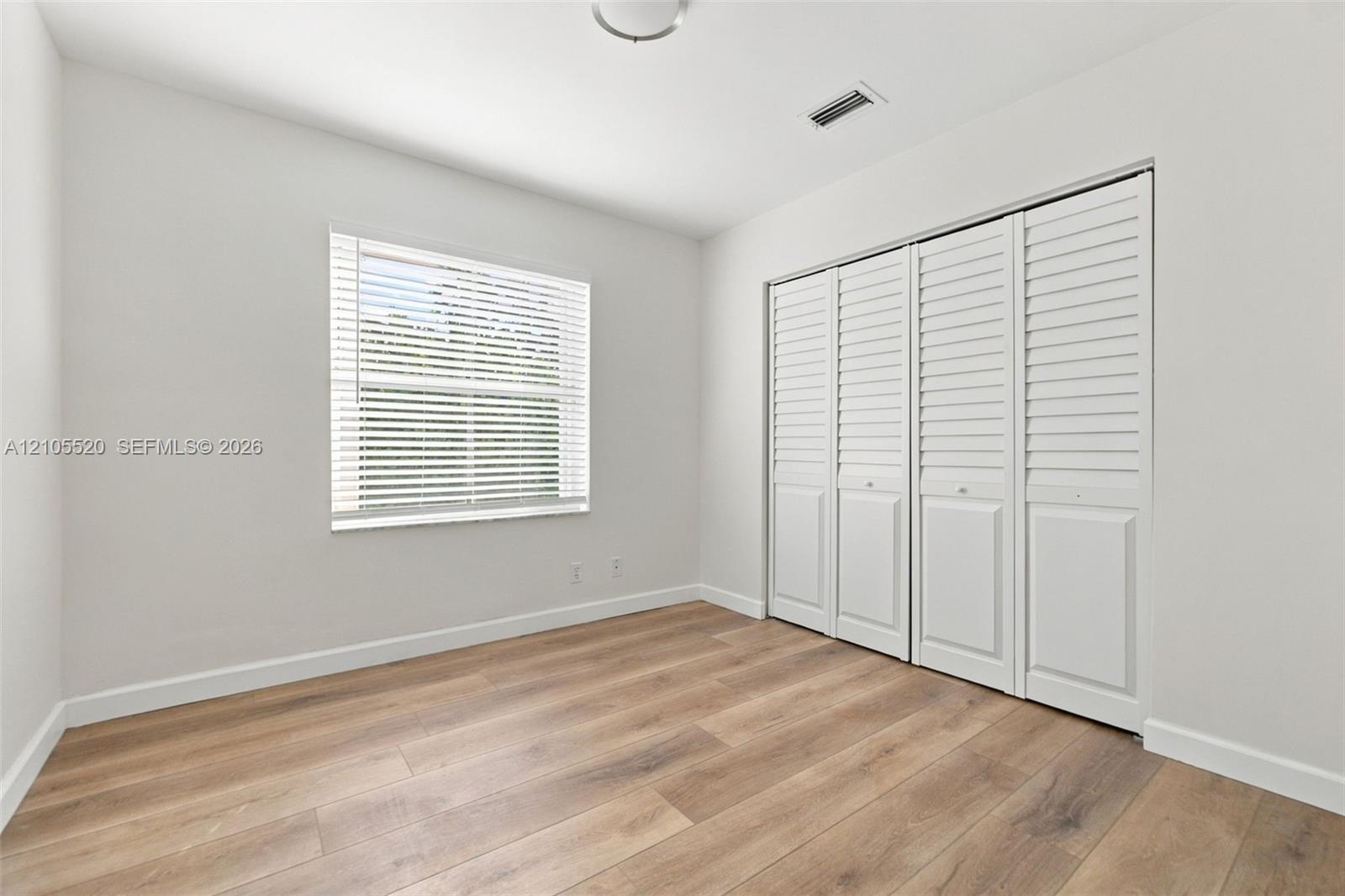 Interior room featuring wood-finish flooring, a single-panel window with horizontal blinds, and a built-in four-panel louvered closet door