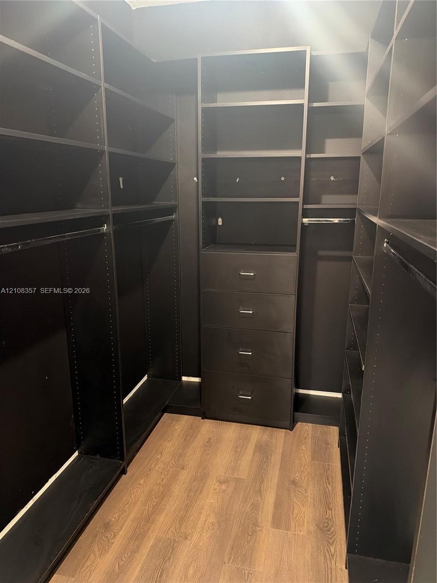 Walk-in closet featuring floor-to-ceiling built-in cabinetry, integrated shelving units, a four-drawer dresser cabinet, metal hanging rods, and wood-f