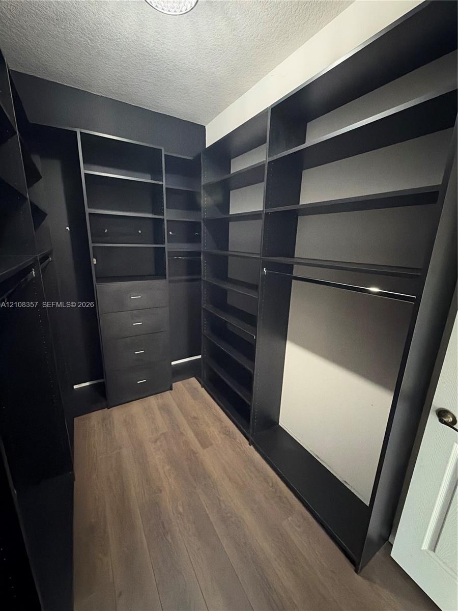 Custom walk-in storage featuring dark finish floor-to-ceiling cabinetry, integrated shelving, built-in dresser drawers, and wood-finish flooring