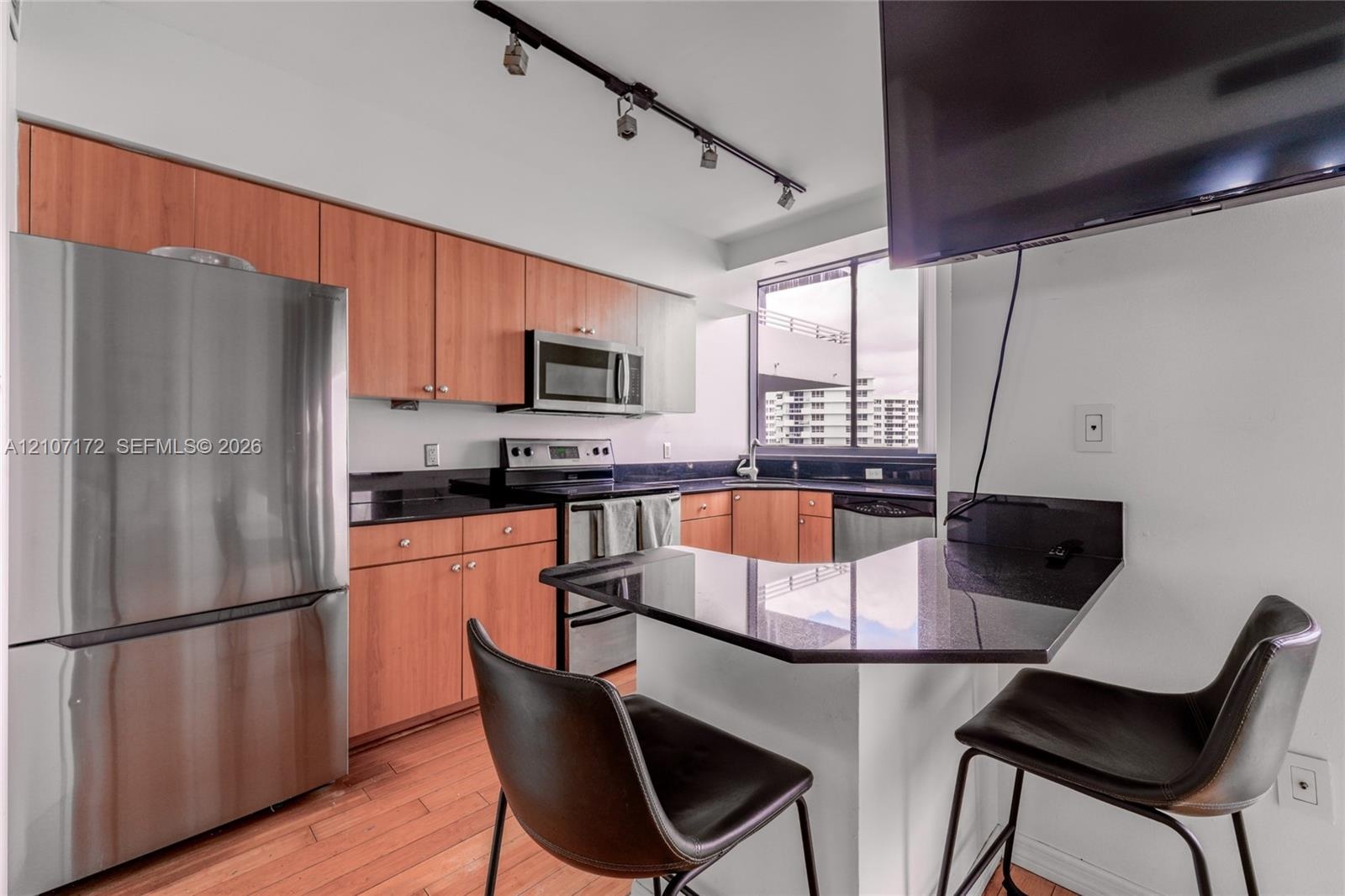 Kitchen featuring wood cabinetry, stainless steel appliances, dark stone-finish countertops, a breakfast bar, and track lighting
