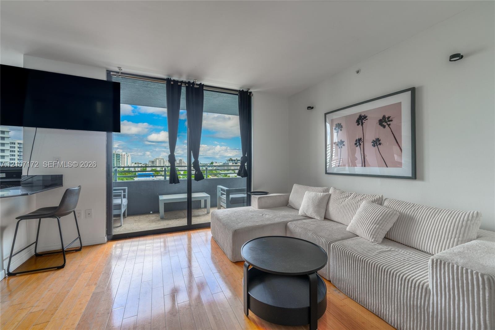 Floor-to-ceiling sliding glass doors, built-in stone-surface breakfast bar, wood-finish flooring, and private balcony