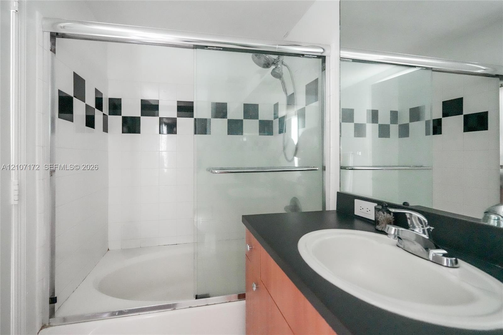 Bathroom featuring a tub-shower combination with glass sliding doors and a decorative black-and-white checkered tile accent, paired with a vanity cont