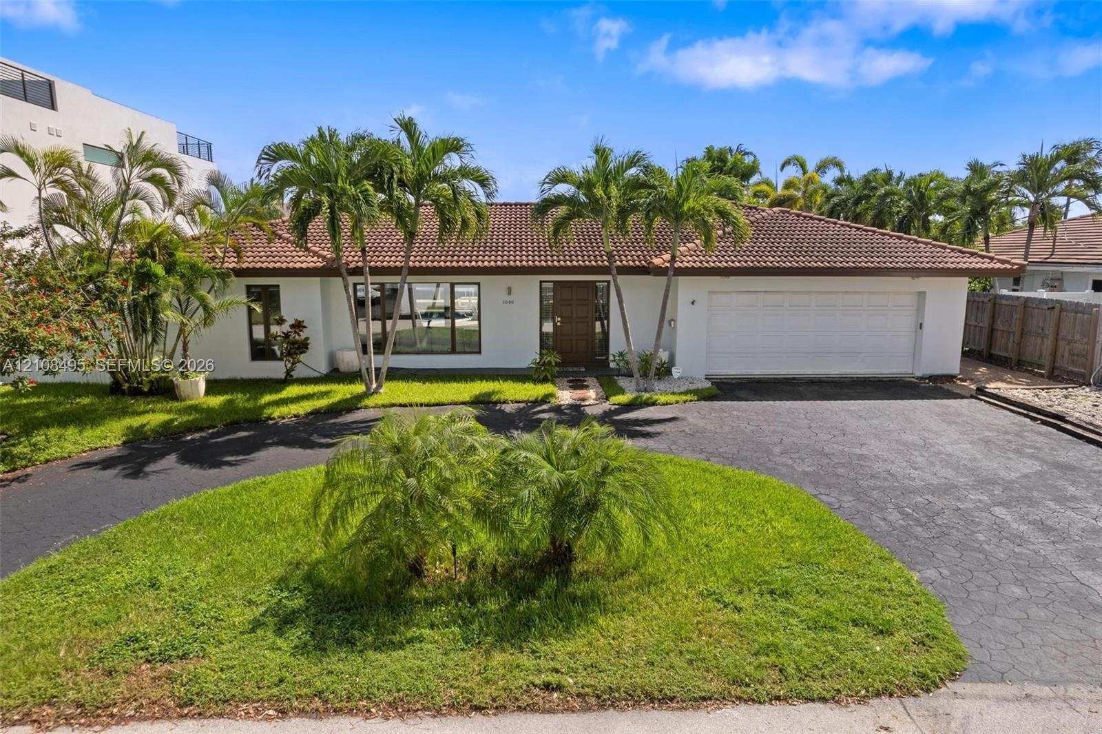 Single-story exterior featuring white stucco siding, a tiled roof, a multi-car garage, and a paved circular driveway