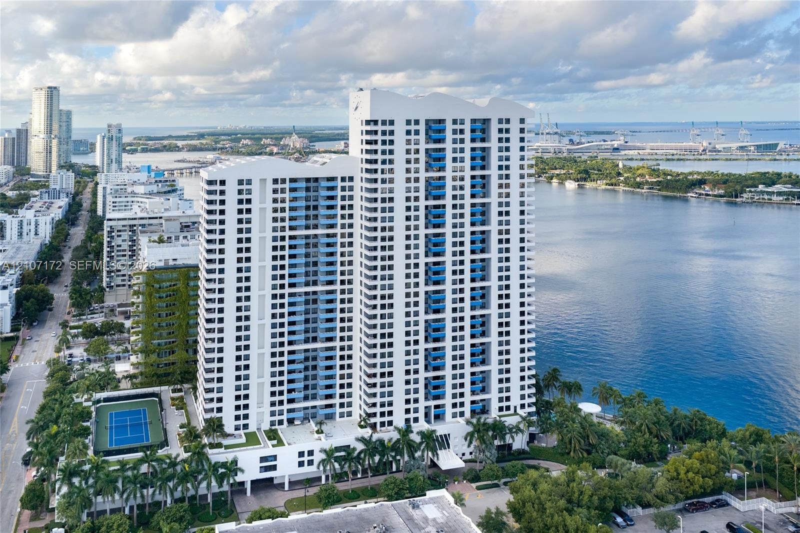 Aerial perspective featuring a glass-facade high-rise tower, expansive coastal waterfront, and urban skyline