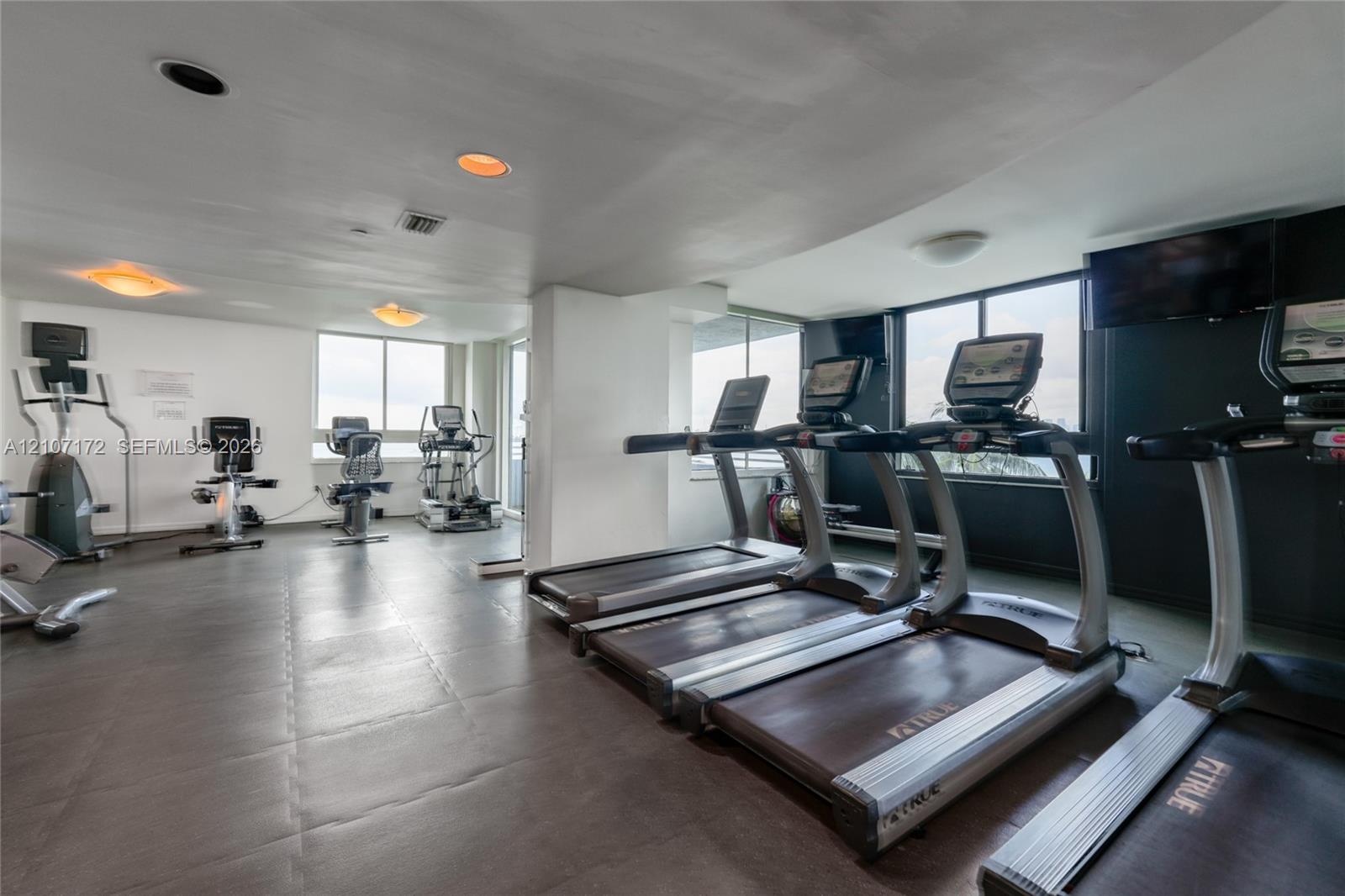Fitness center featuring wood-finish flooring, full-length wall mirrors with wood frames, and glass-paneled double doors