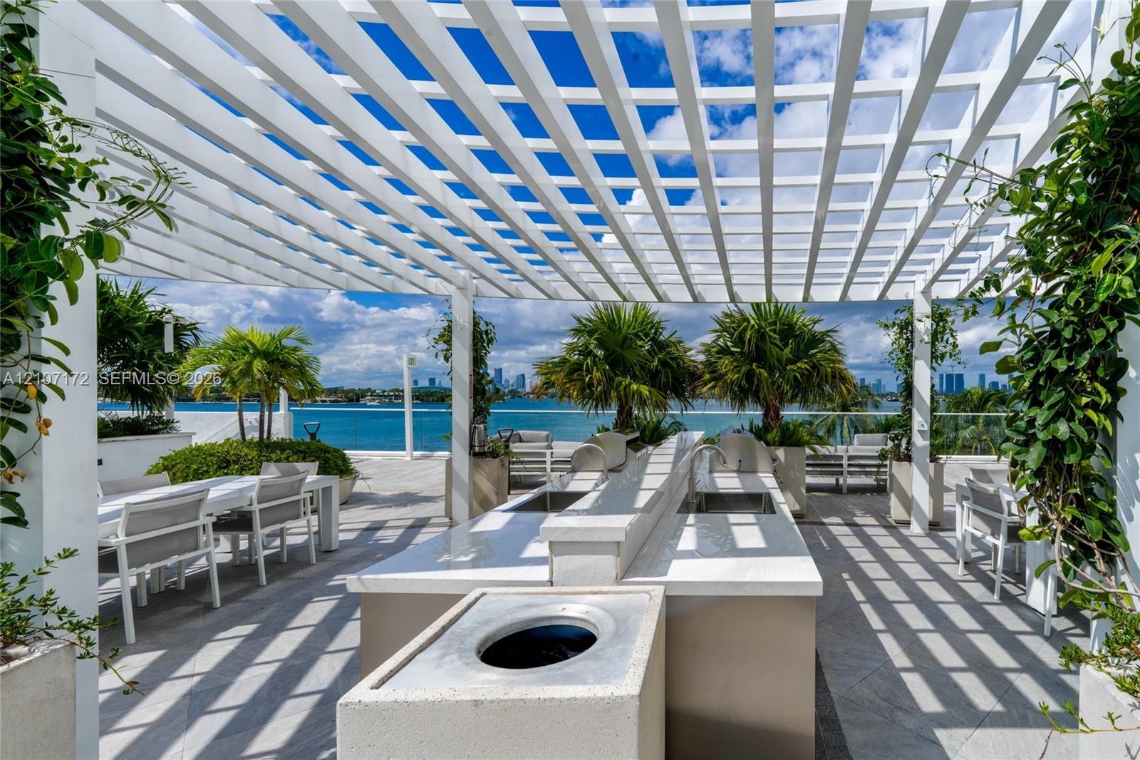 Outdoor terrace featuring a white pergola, stainless steel built-in grill, stone-surface countertop, and large planters