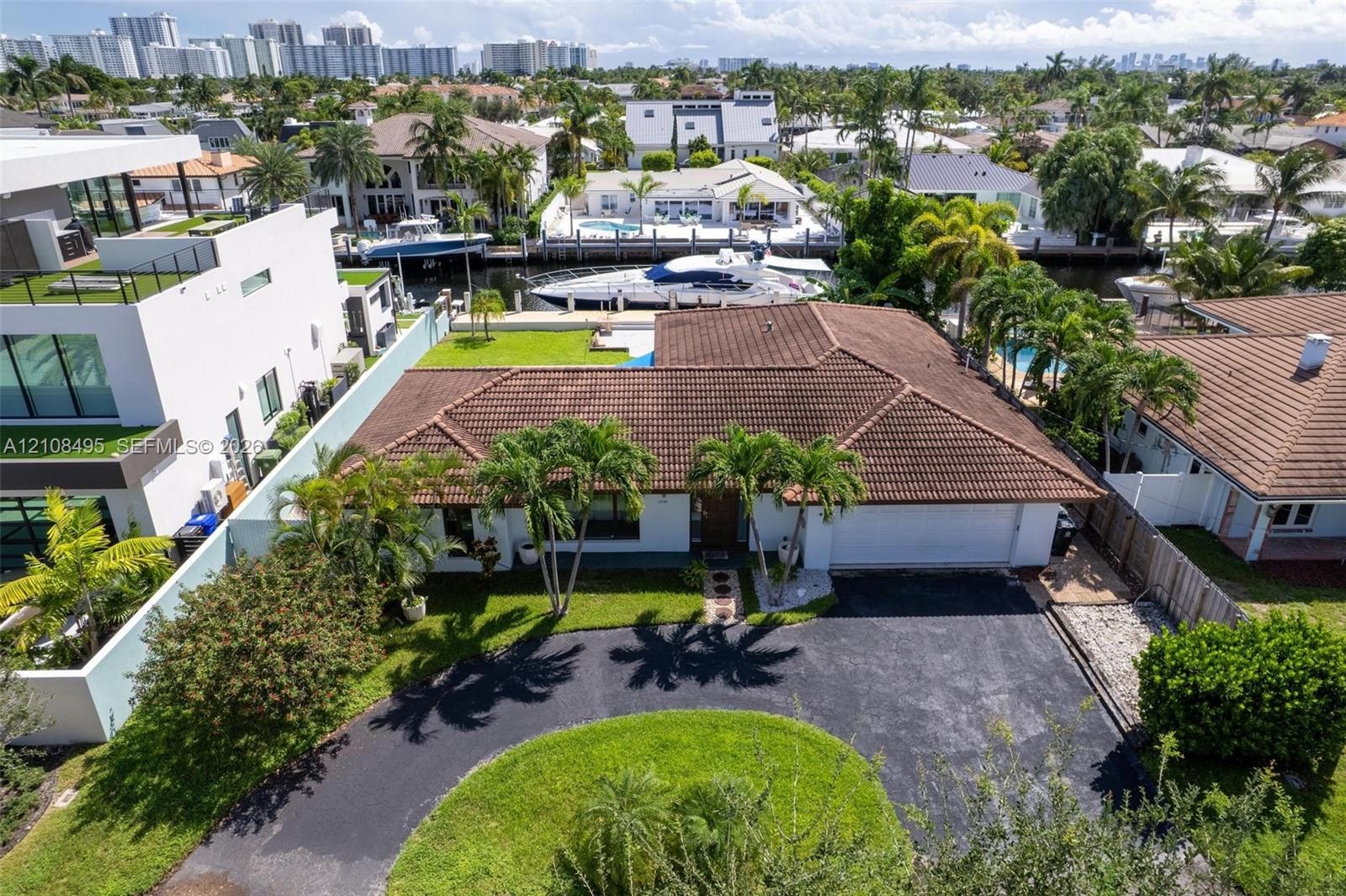 Aerial perspective of a waterfront property featuring a canal-front bulkhead, private swimming pool, concrete patio, paved driveway, and tile roof