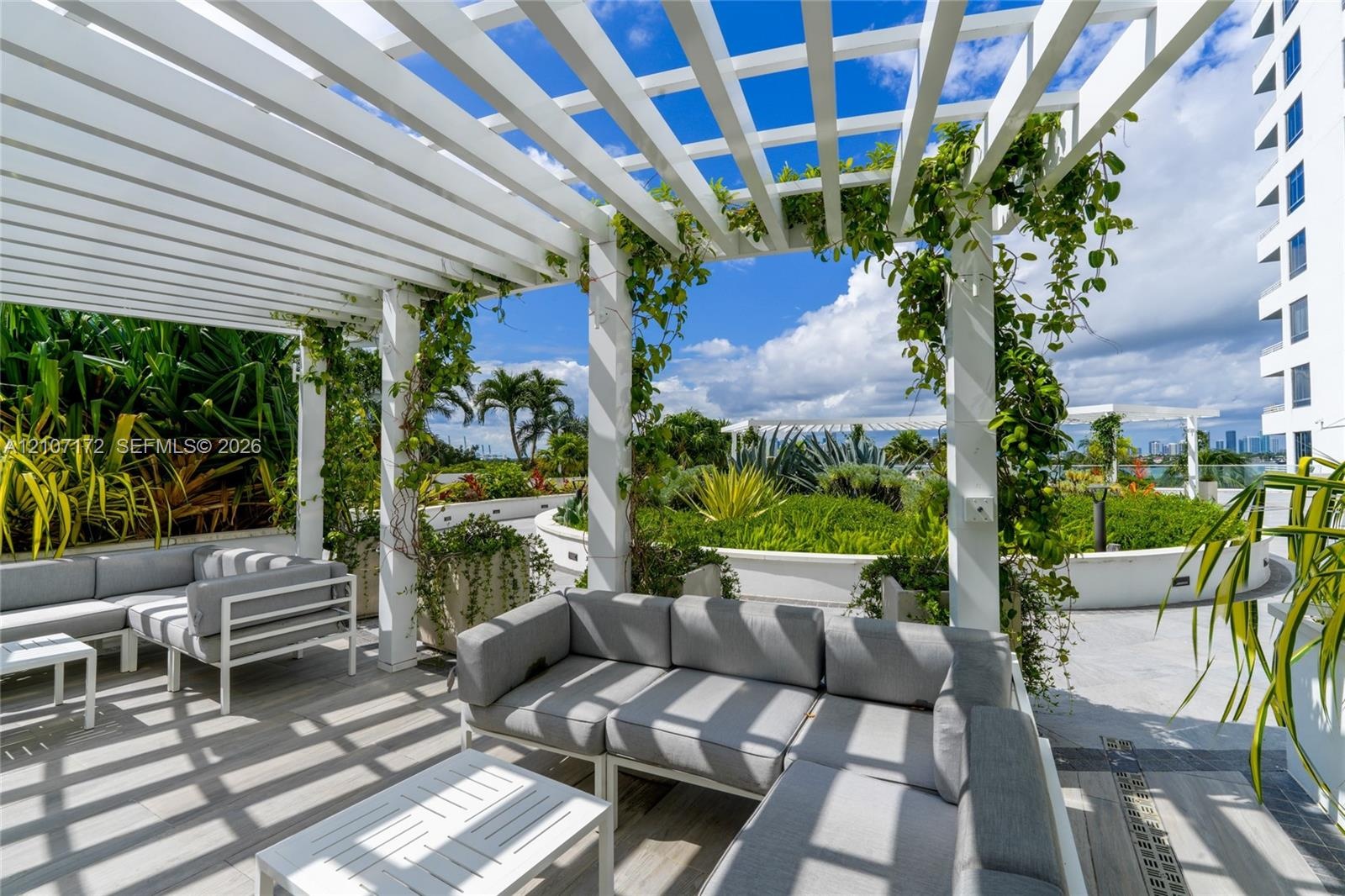 Outdoor terrace featuring a white overhead trellis, built-in stainless steel kitchen station, stone-surfaced flooring, and perimeter planters