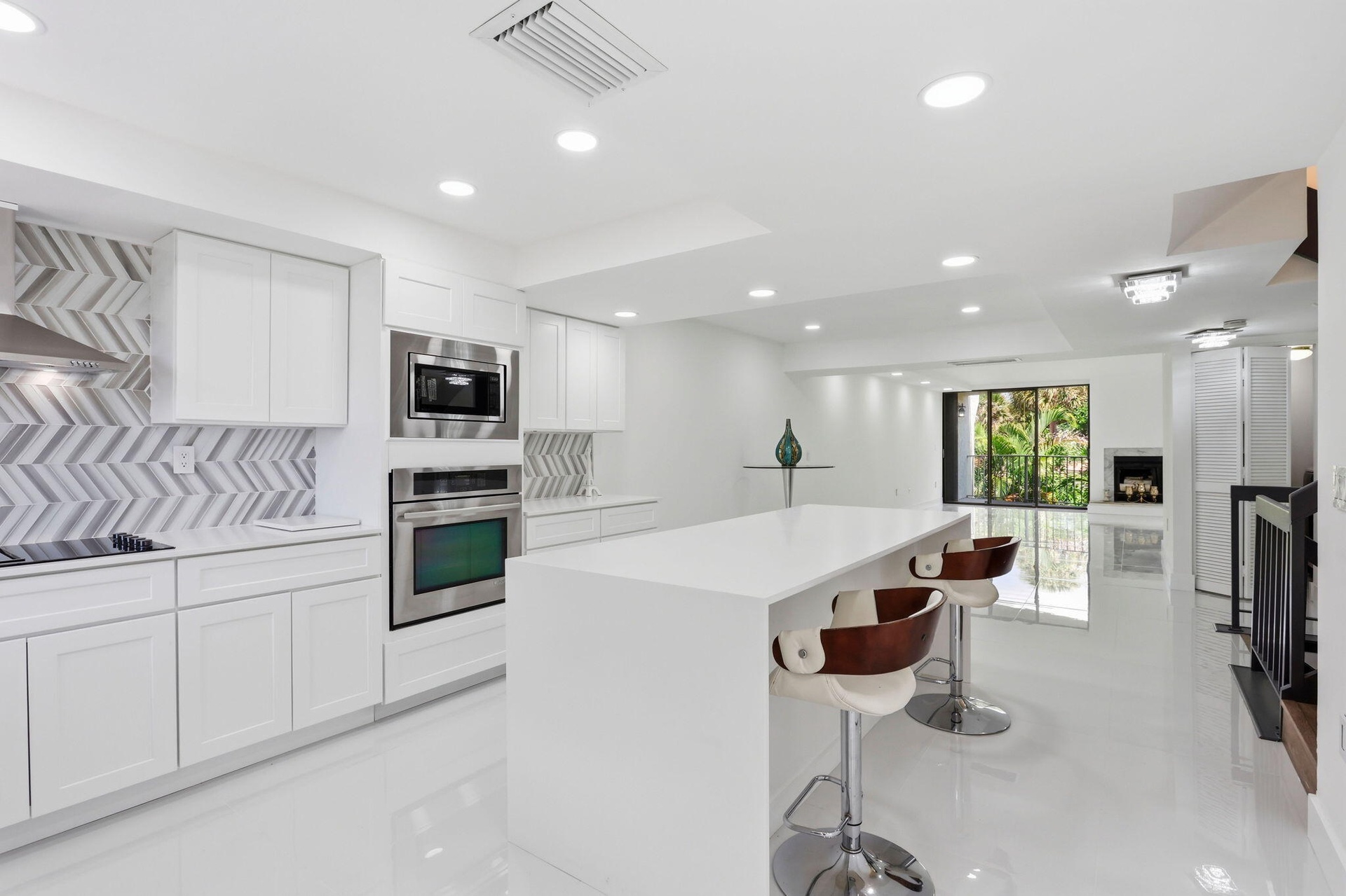 White shaker cabinetry, stainless steel appliances, herringbone tile backsplash, recessed lighting, and a kitchen island with a white countertop