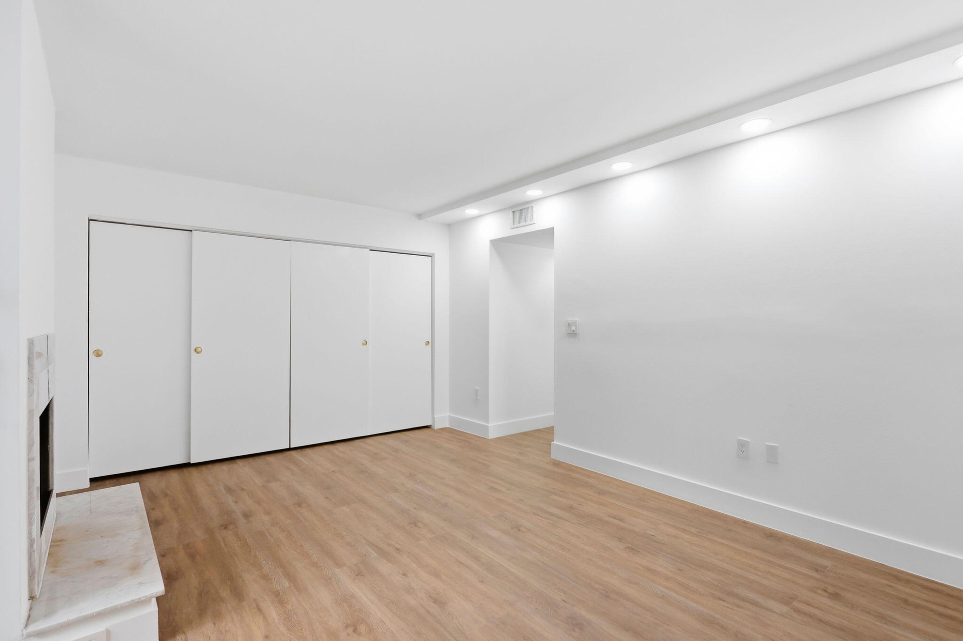 Recessed lighting, wood-finish flooring, white walls, built-in closet with sliding doors, and a fireplace with a stone surround
