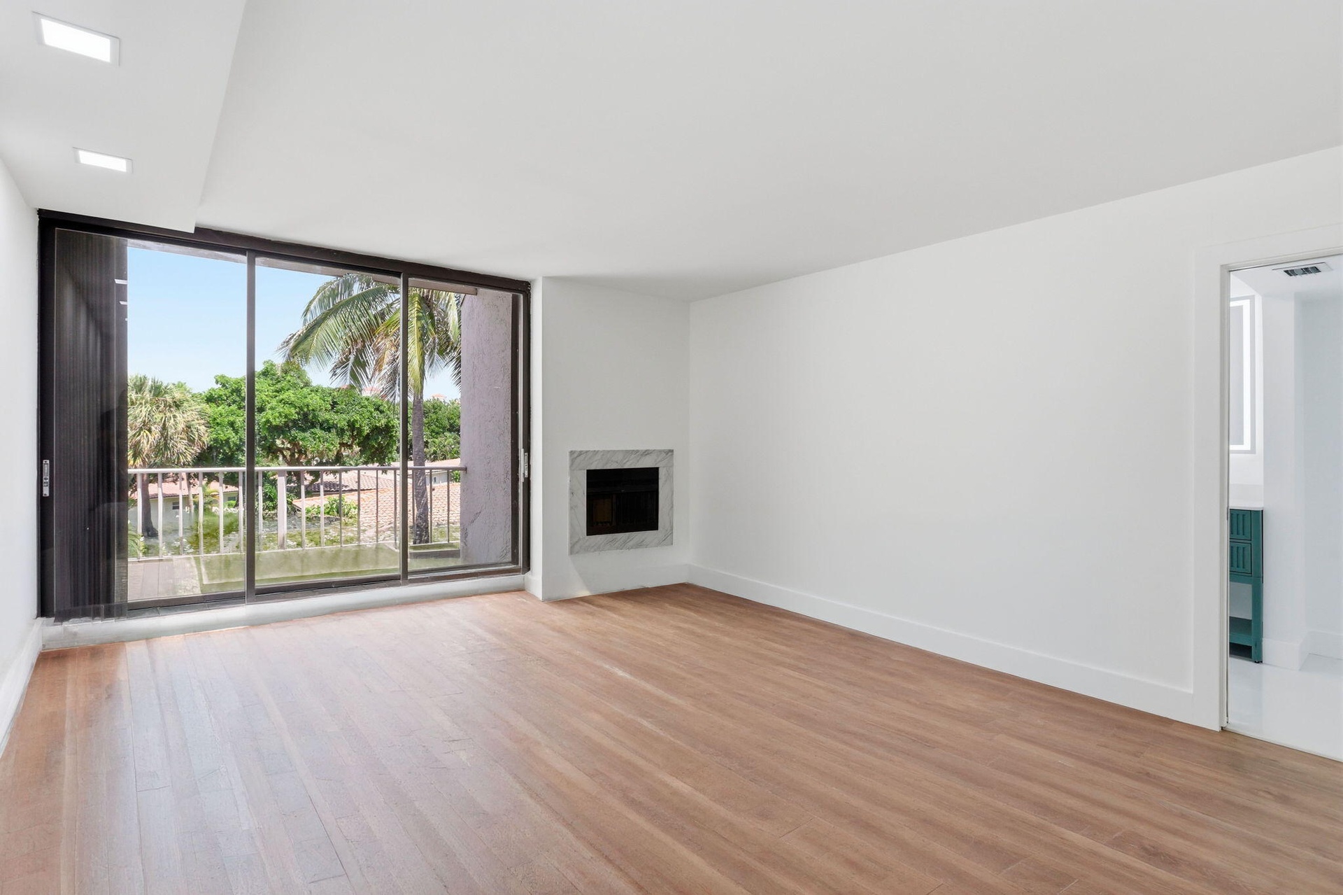 Wood-finish flooring throughout, recessed ceiling lighting, a built-in fireplace with a stone surround, and an expansive sliding glass door to the ext
