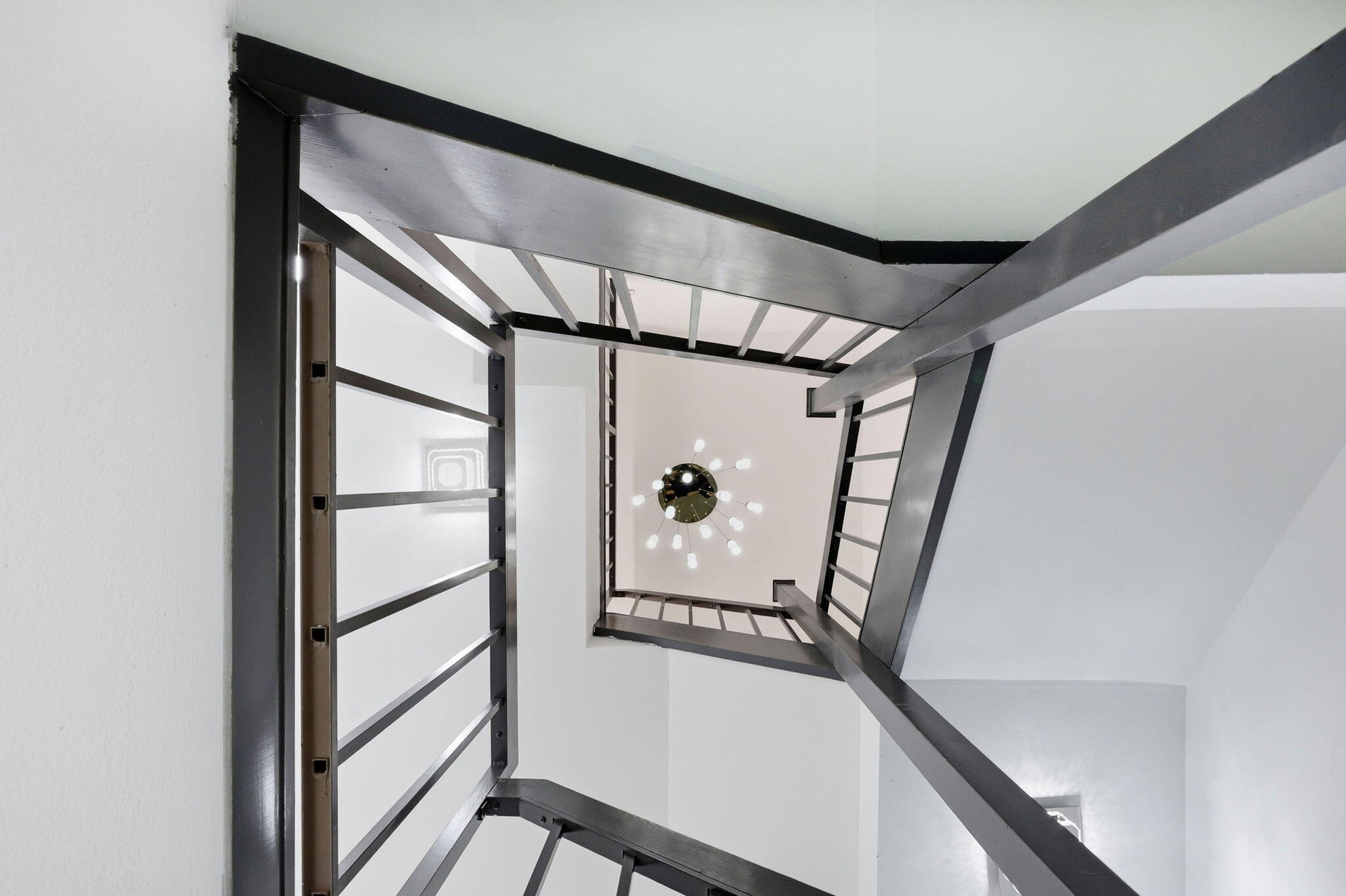 Architectural staircase with metal railings, white walls, and a multi-bulb ceiling fixture