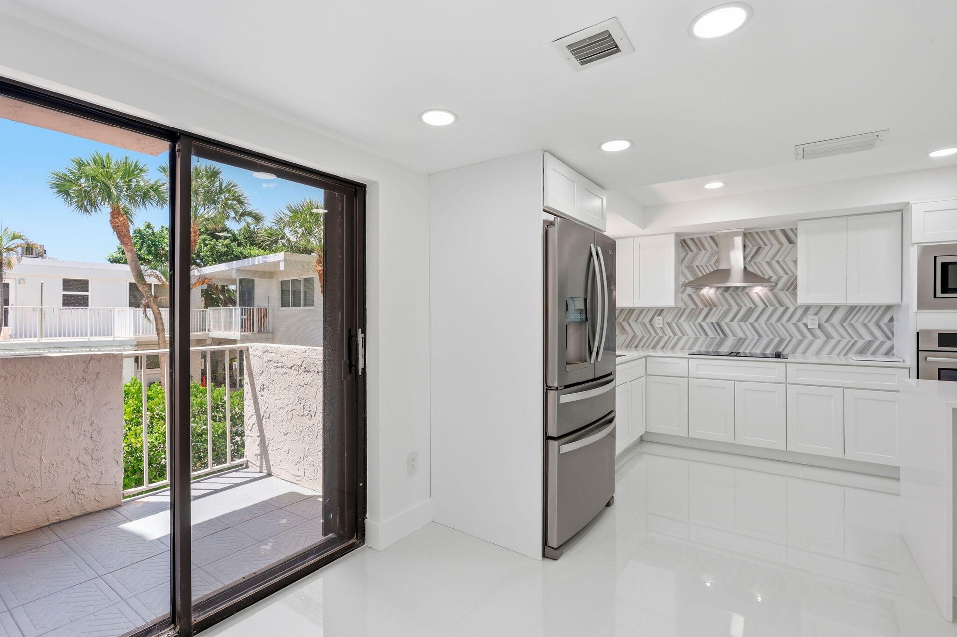 Modern kitchen featuring white cabinetry, stainless steel appliances, and a herringbone tile backsplash, dining area