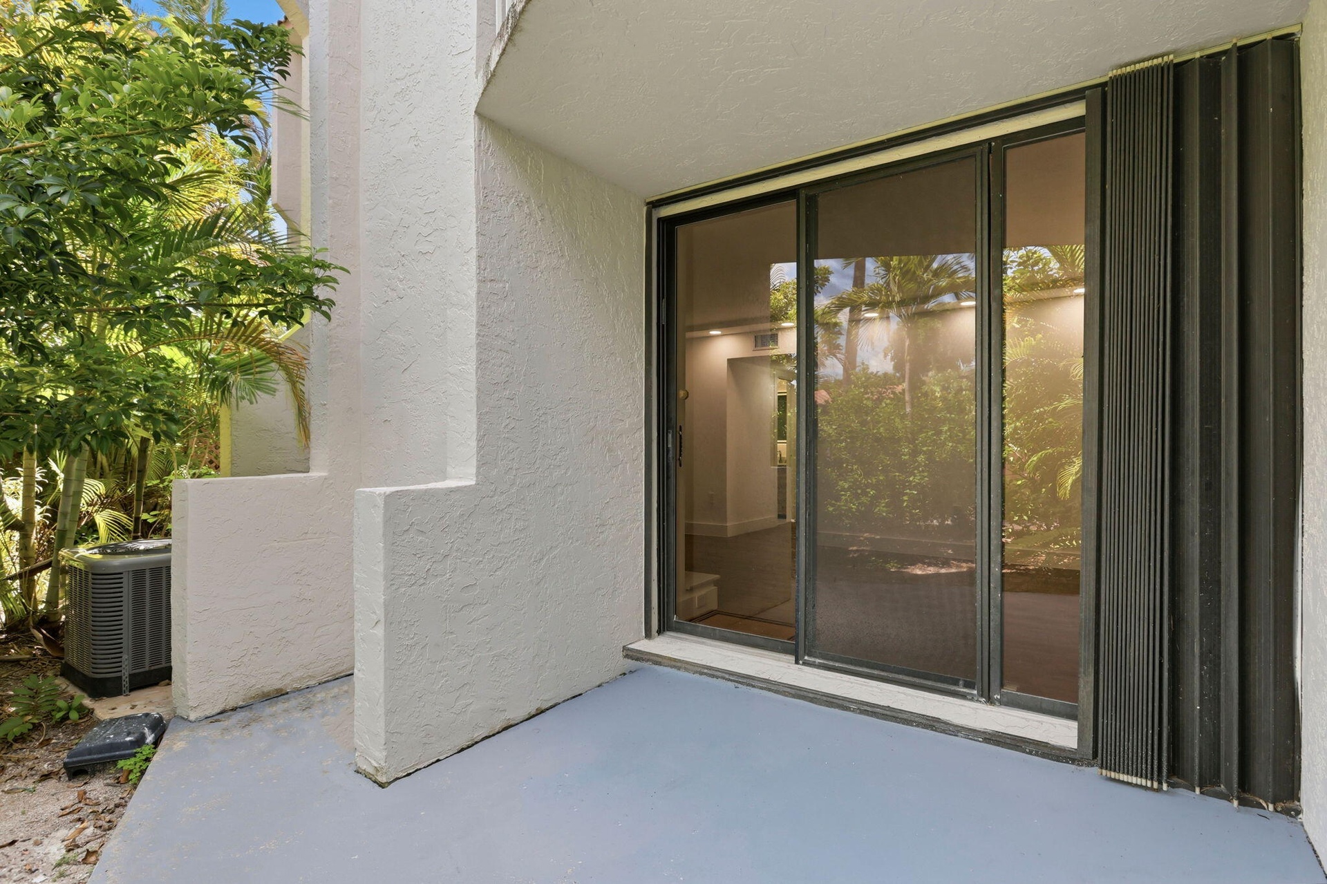 Patio with sliding glass doors, accordion hurricane shutters, and an air conditioning unit