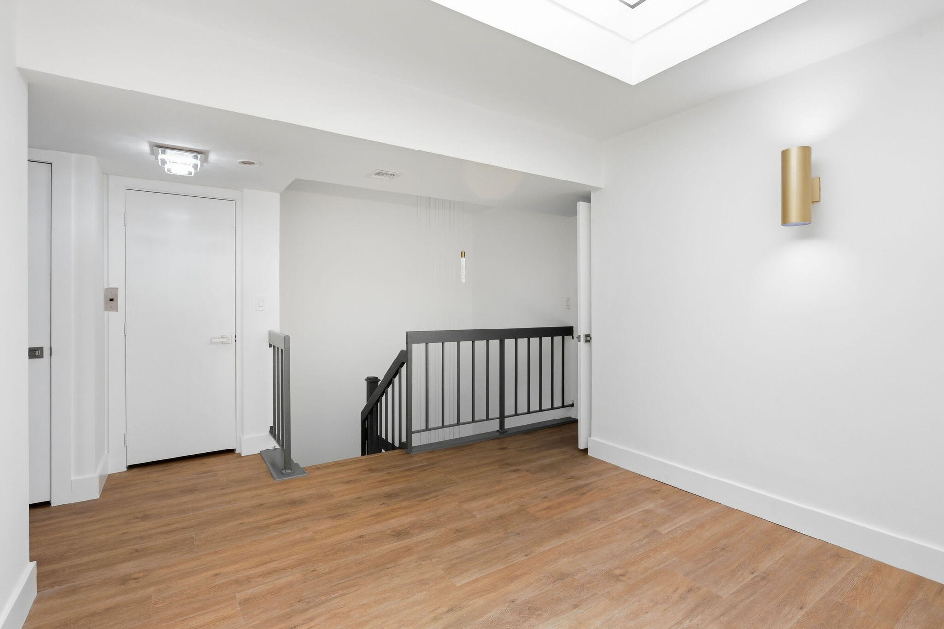 Wood-finish flooring, white walls, and a contemporary brass wall sconce