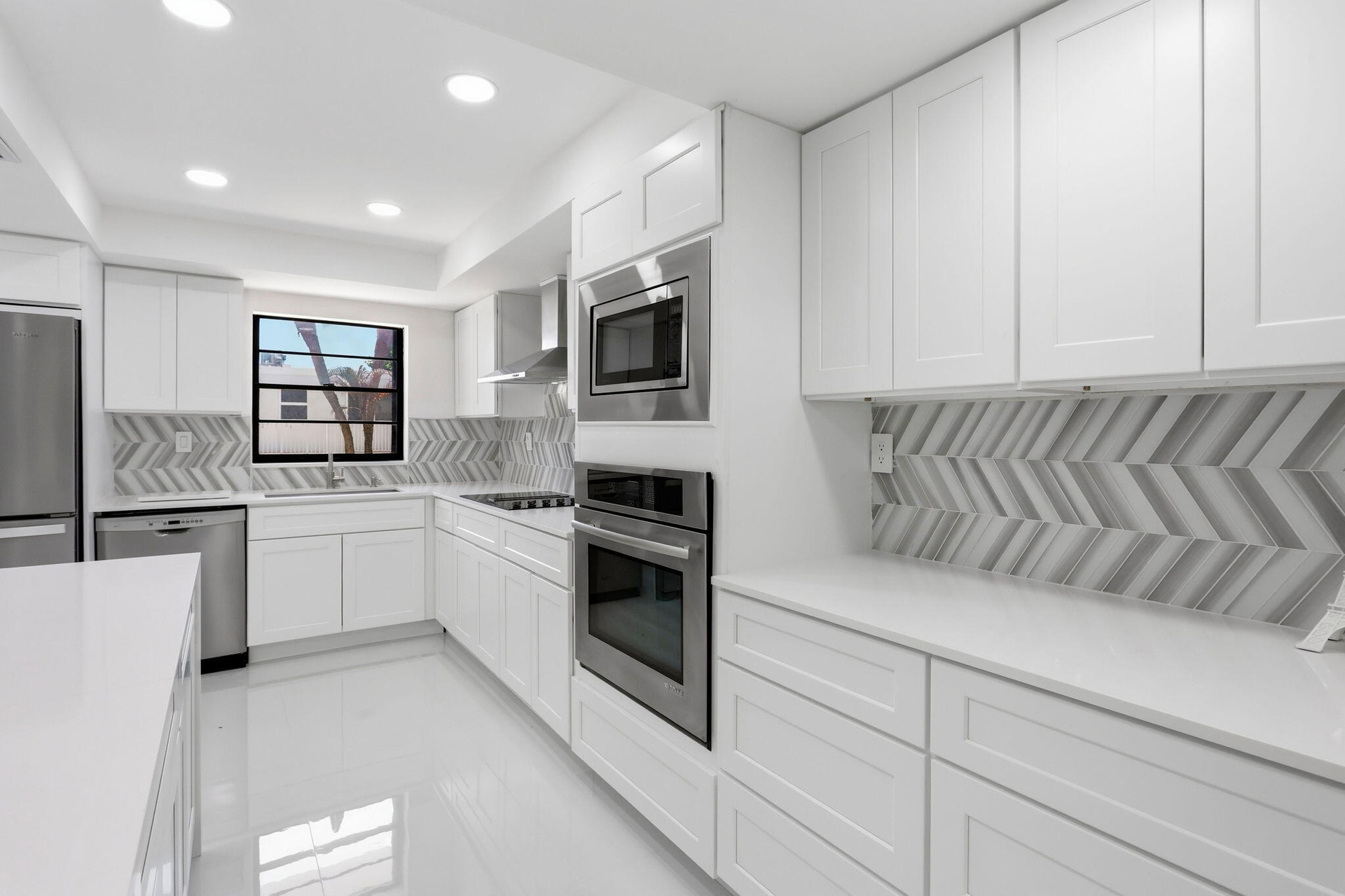 White cabinetry, stainless steel appliances, herringbone-patterned backsplash, recessed lighting, and a window above the sink