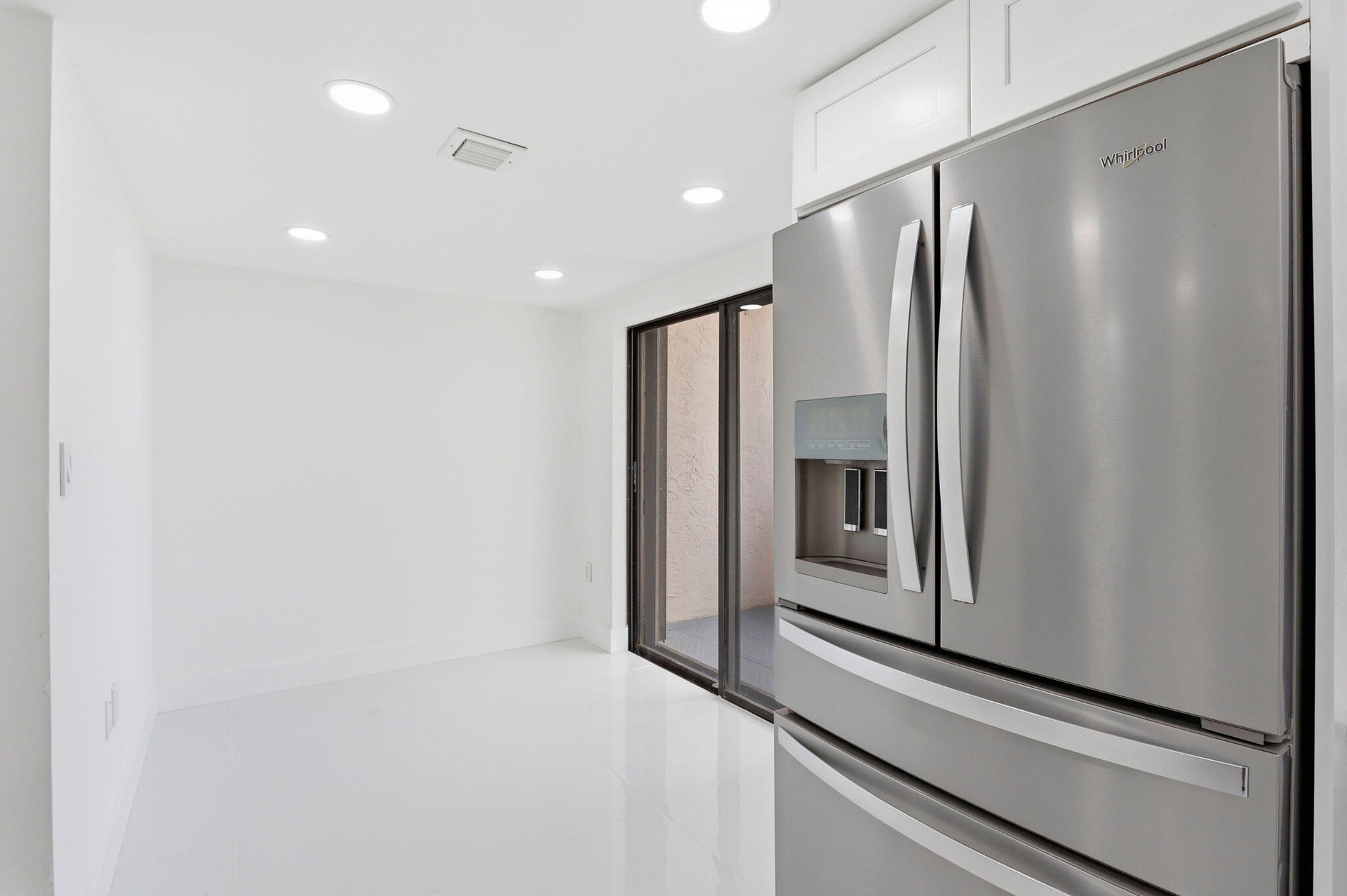 Stainless steel French door refrigerator, white cabinetry, recessed lighting, white flooring, and sliding glass door