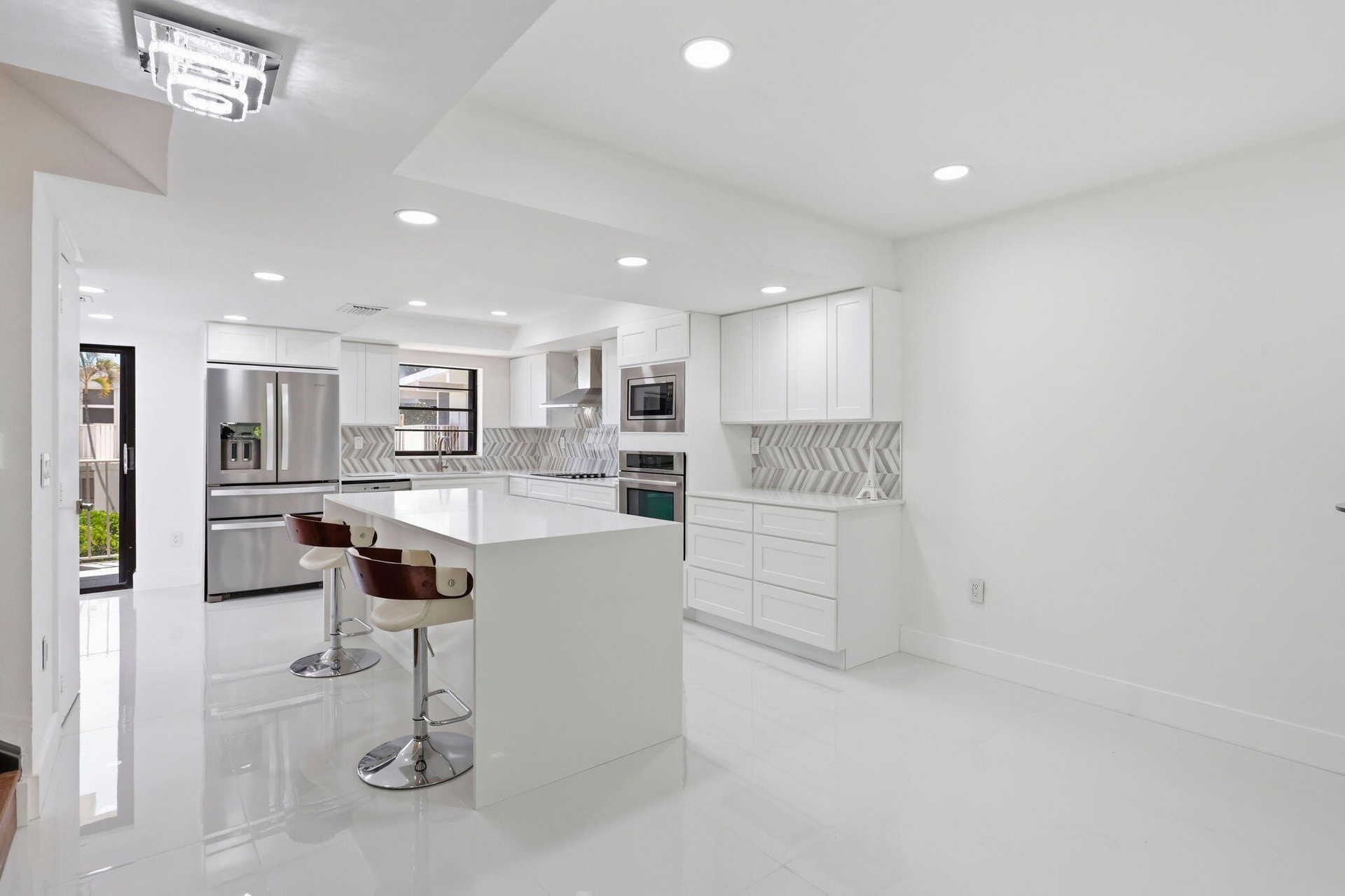 Contemporary kitchen featuring a large island, white cabinetry, stainless steel appliances, and a chevron tile backsplash