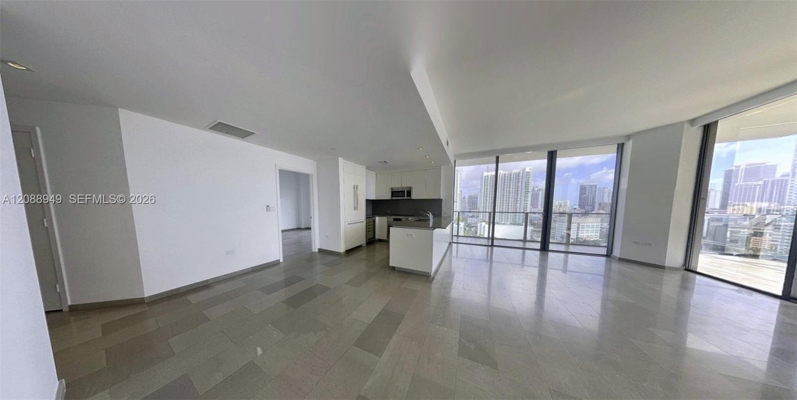 Open-concept interior featuring large-format tile flooring, floor-to-ceiling windows, and a kitchen equipped with a central island and stone-surfaced 