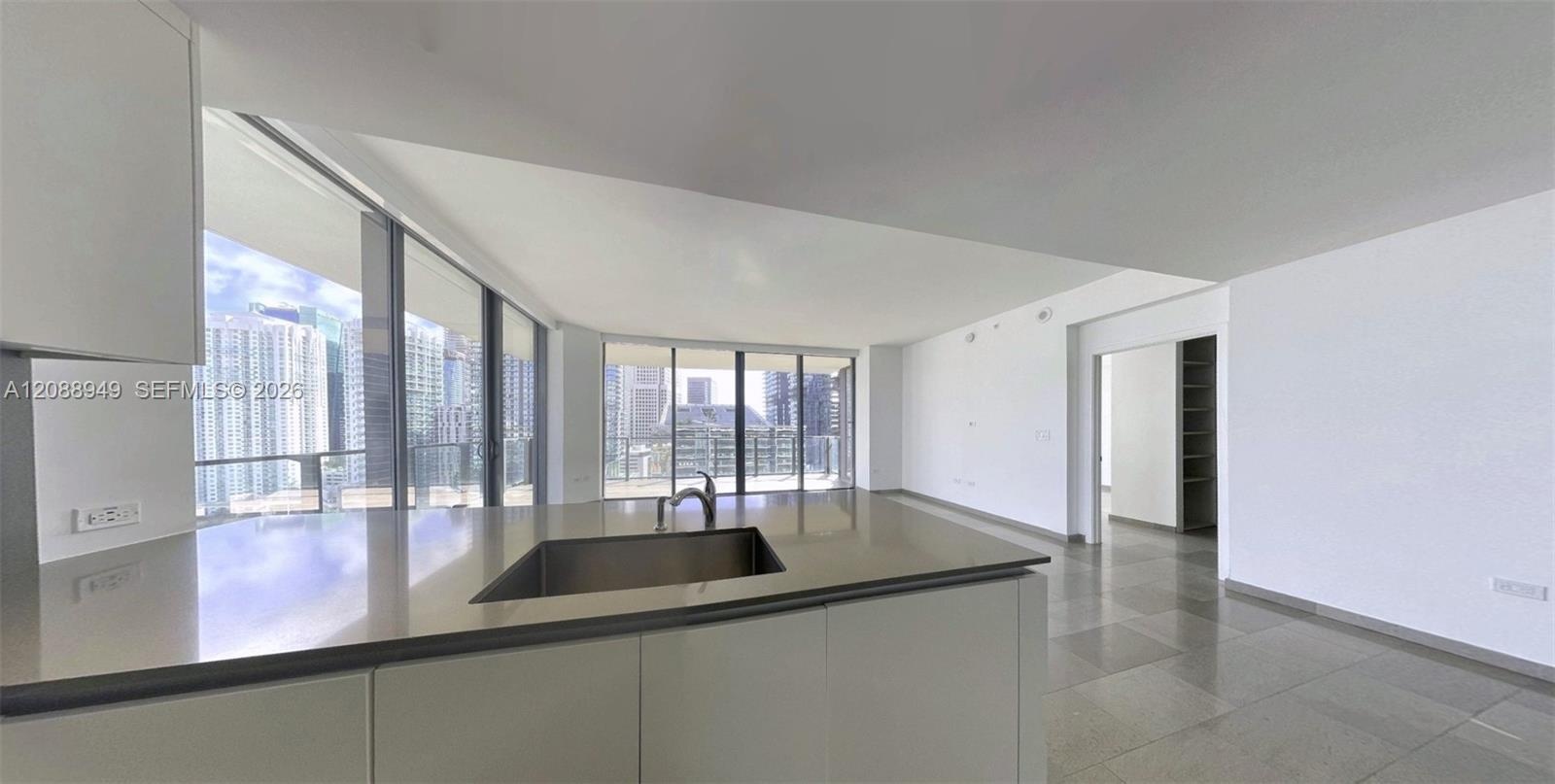 Kitchen island with a solid-surface countertop, under-mount stainless steel sink, flat-panel cabinetry, floor-to-ceiling windows, and large-format til