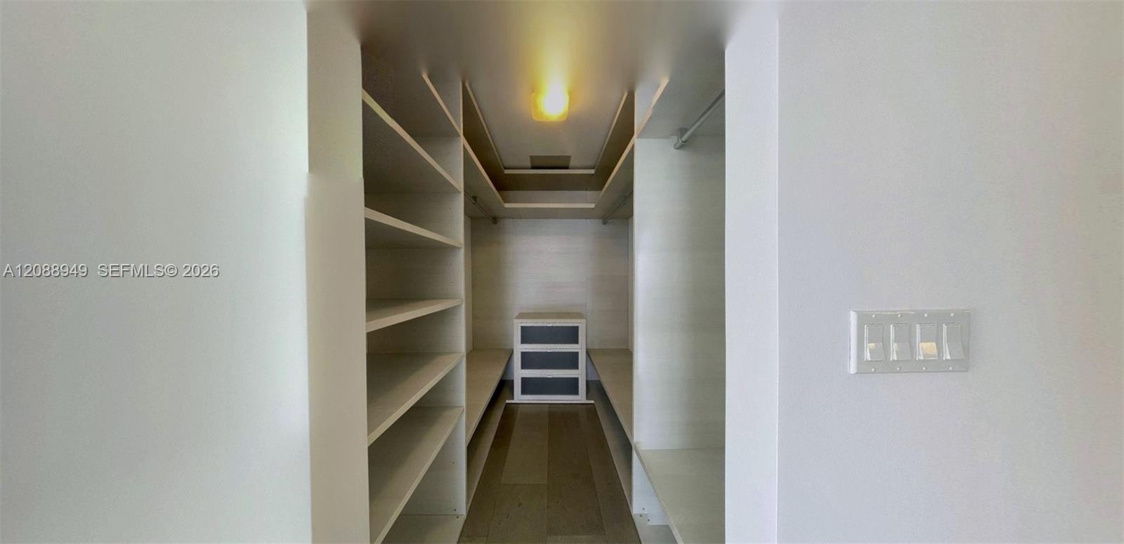 Walk-in closet featuring floor-to-ceiling built-in shelving, multiple hanging rods, and wood-finish flooring
