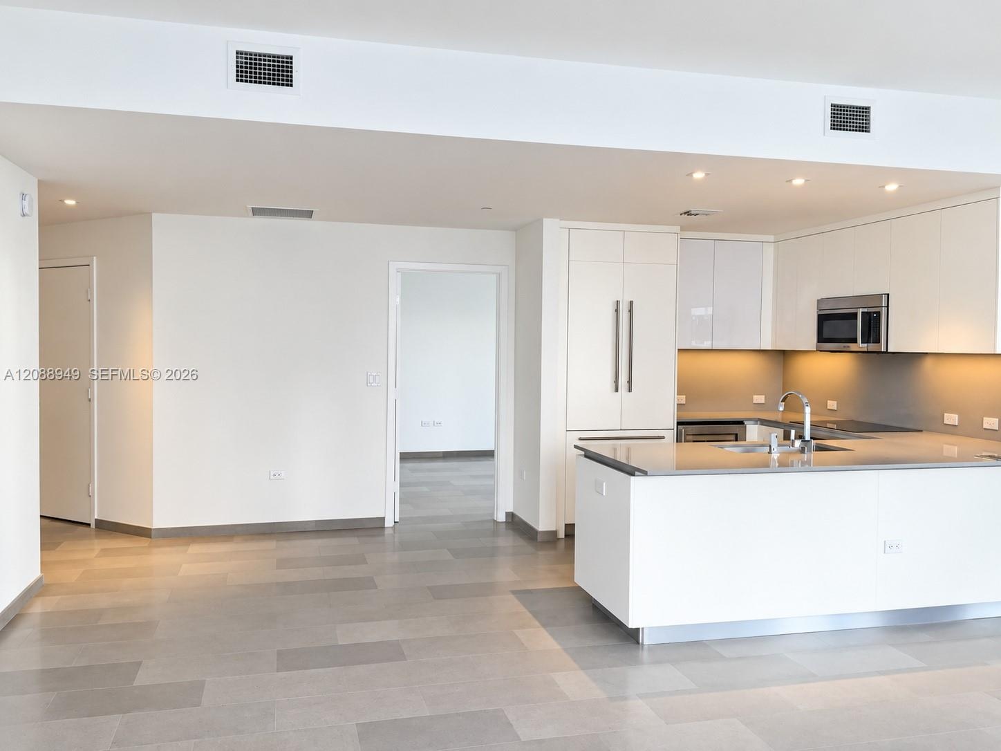 Modern kitchen featuring white flat-panel cabinetry, a central island with a solid-surface countertop, stainless steel appliances, and neutral-tone ti