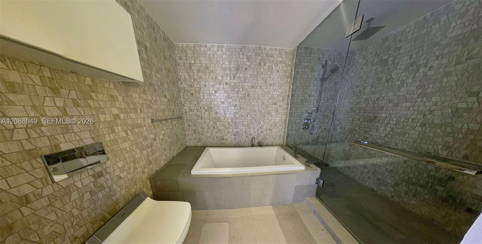 Built-in soaking tub with a tiled surround, glass-enclosed walk-in shower, wall-mounted rainfall showerhead, mosaic tile accent walls, and large-forma