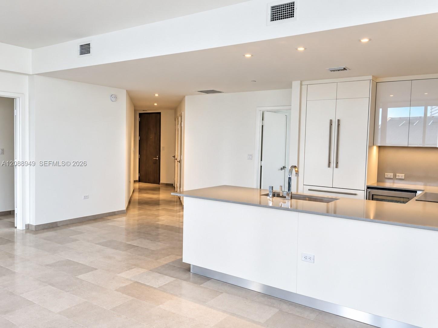 Modern kitchen featuring white flat-panel cabinetry, stone-finish countertops, recessed lighting, and large-format tile flooring