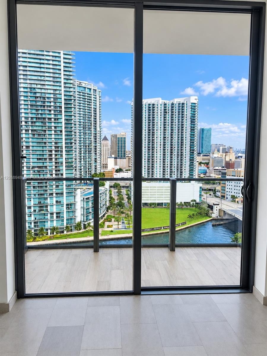 Full-height sliding glass doors with dark metal frames, wood-finish flooring, and a private balcony featuring a glass panel railing