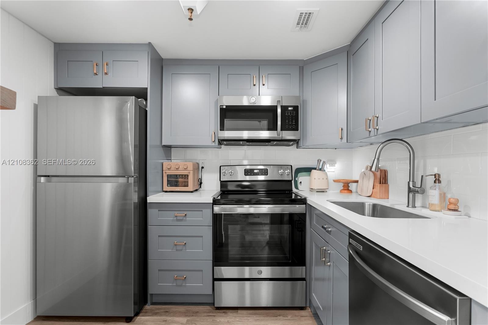 Kitchen featuring shaker-style cabinetry with metallic hardware, white solid-surface countertops, subway tile backsplash, and stainless steel applianc