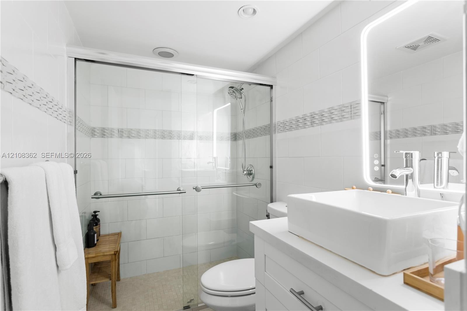 Walk-in shower with sliding glass doors, white subway-style wall tiling, decorative mosaic tile inlay, modern vessel sink with chrome faucet, and inte